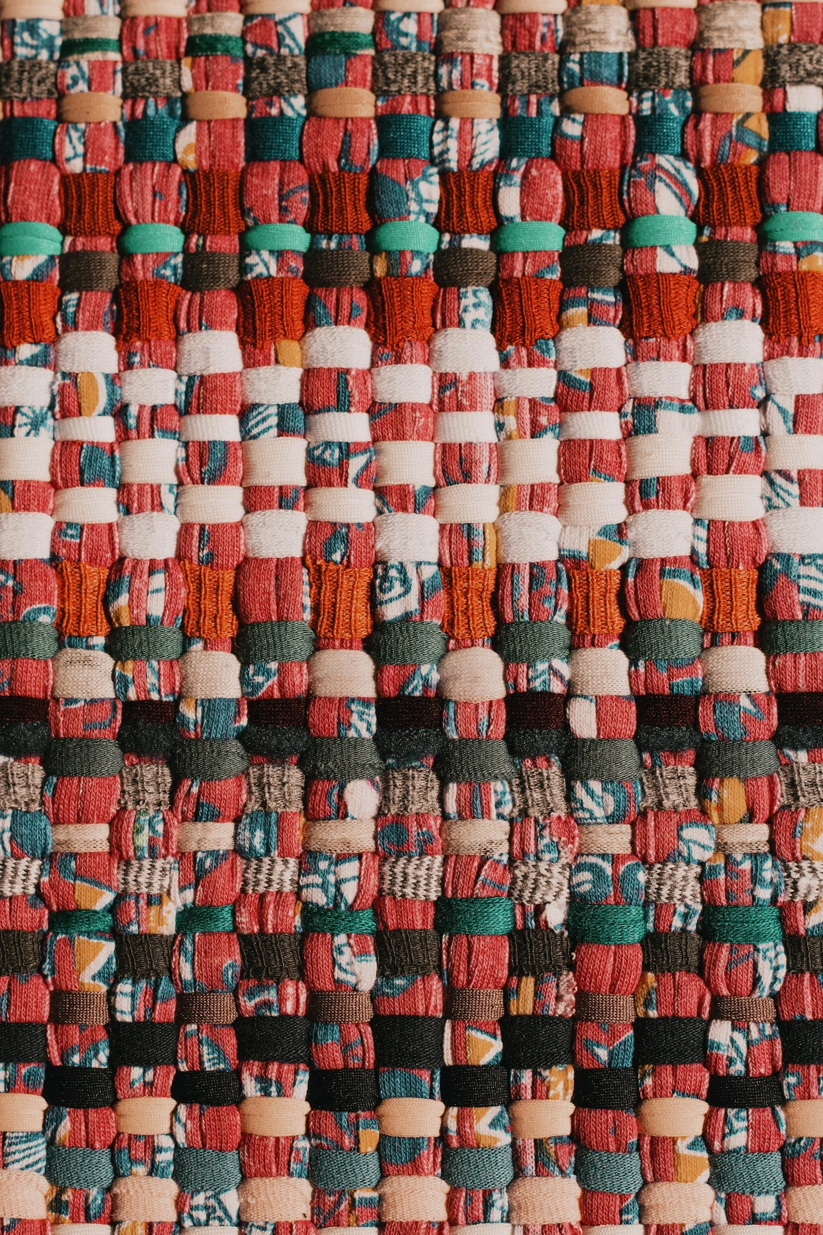 Close-up of a woven fabric with multicolored strips of fabric interlaced in a grid pattern, featuring red, white, black, green, orange, and blue colors.