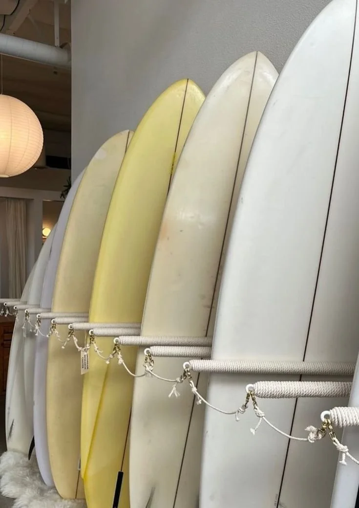 Multiple surfboards arranged vertically on racks in a shop, with a beige paper lantern hanging in the background.