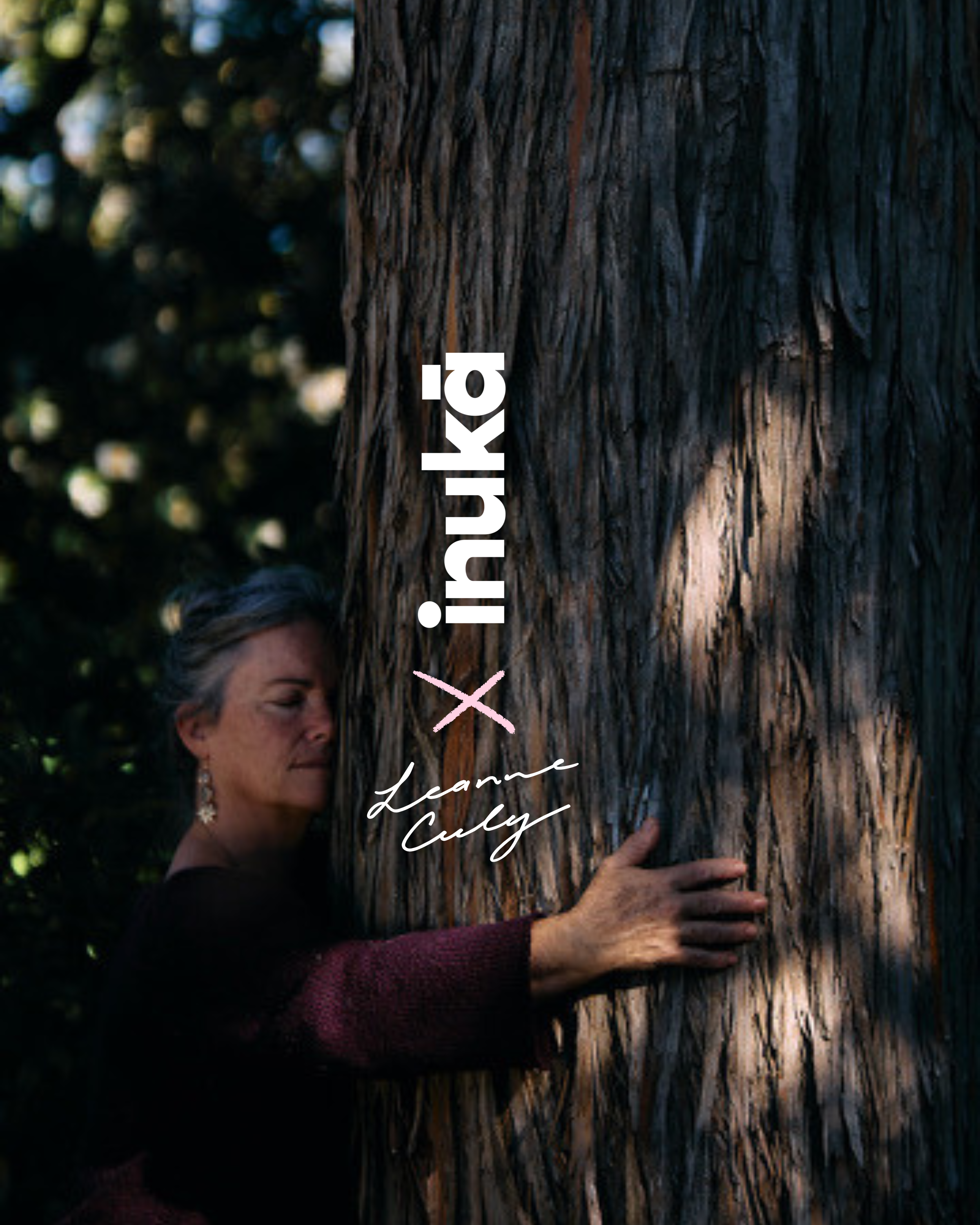 A woman is hugging a large tree trunk outdoors with sunlight filtering through the leaves in the background.
