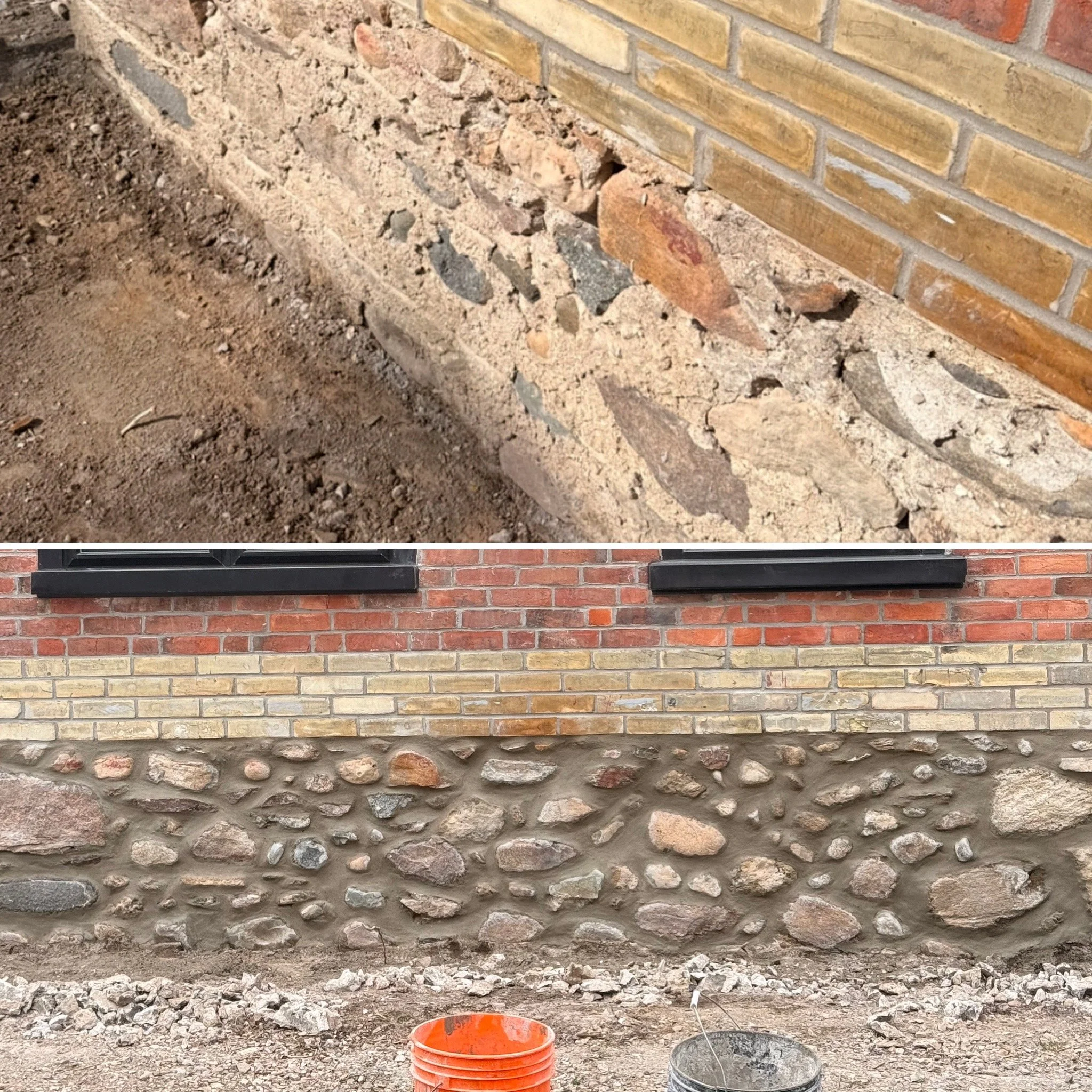 Close-up of a brick wall under construction with a layer of mortar, dirt, and rocks in front. An orange bucket and a gray bucket are placed on the ground near the wall.