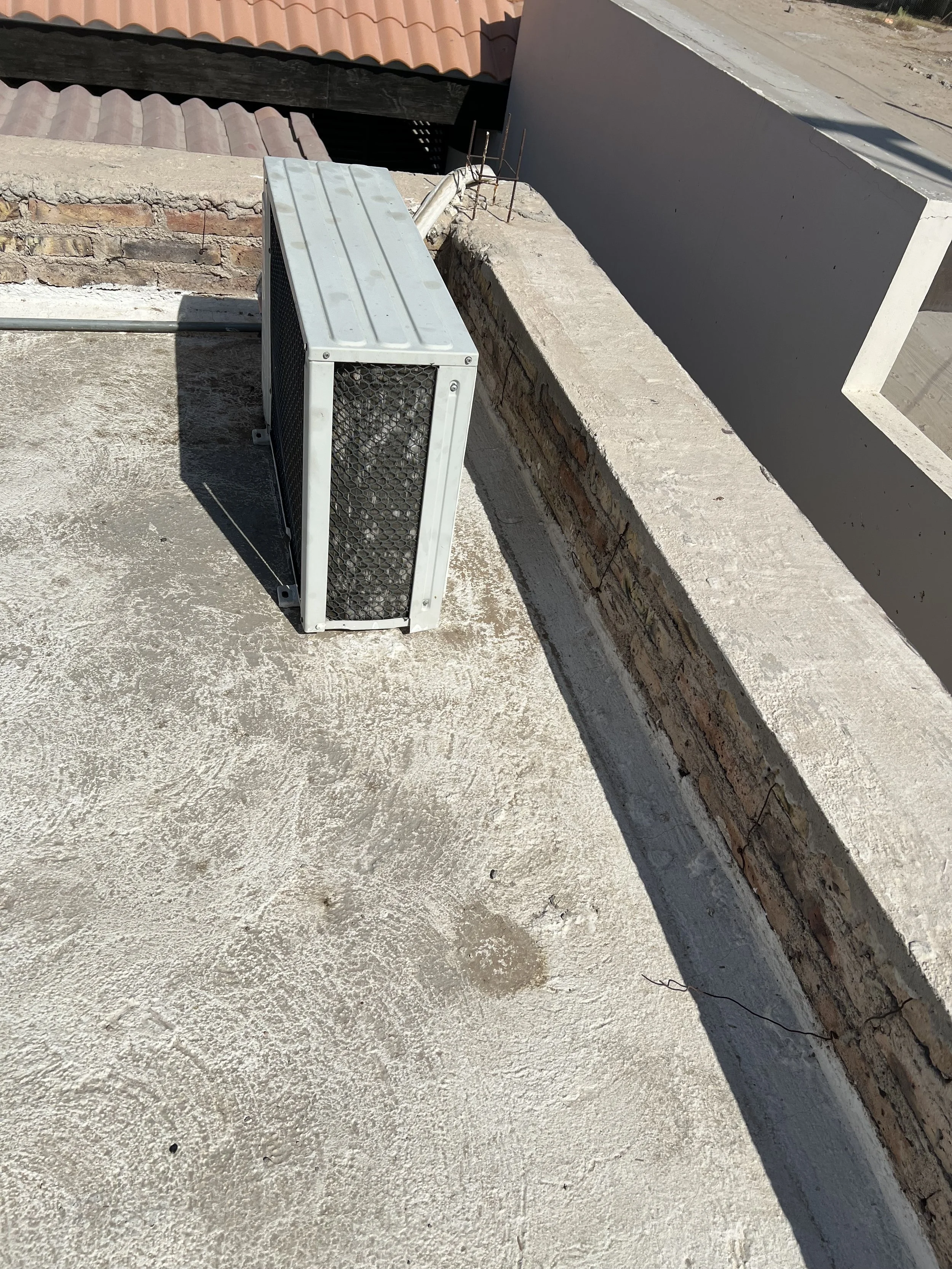 Close-up of a rooftop with an air conditioning unit, brick parapet wall, and red clay roof tiles, roof construction details, shadows, and textures.