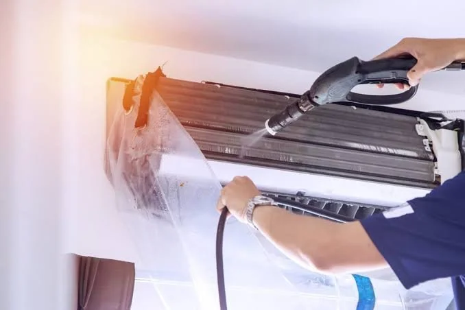 Technician cleaning an air conditioning unit with a vacuum cleaner.