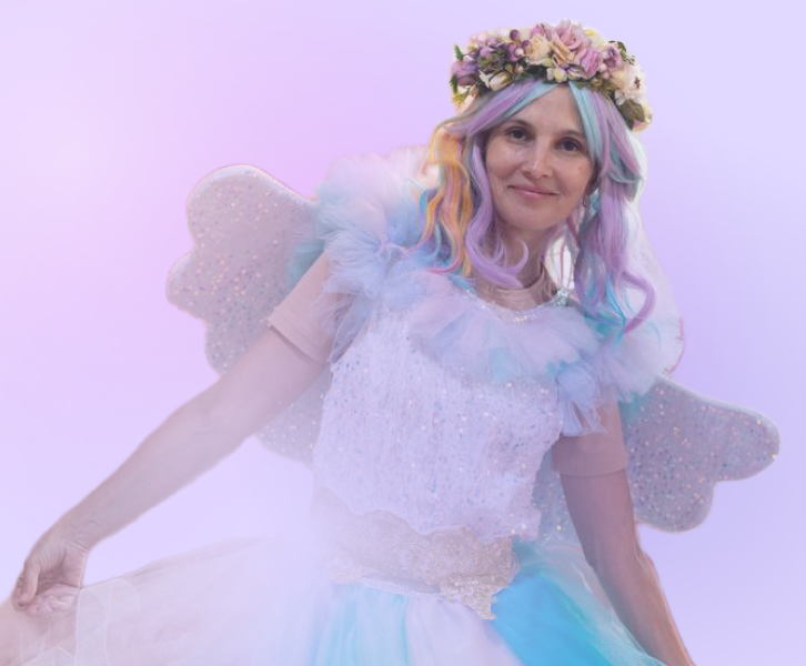 A woman dressed as a fairy with rainbow-colored hair, wearing a flower crown, a pastel dress with glitter, and fairy wings on a light purple background.