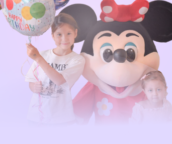 Girl holding a balloon with birthday greetings beside a person dressed in a Minnie Mouse costume and another young girl, both celebrating a birthday.