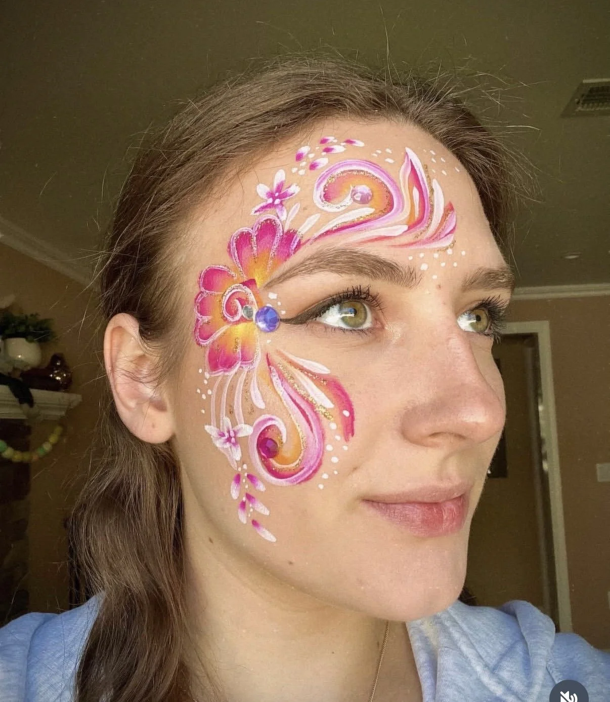 Colorful pink floral face painting design with swirls and decorative details.