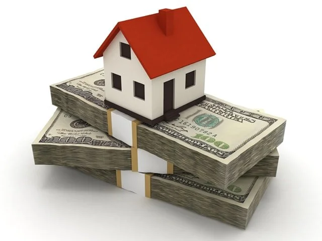 A small house model on top of stacks of hundred-dollar bills, illustrating real estate investment or mortgage concept.