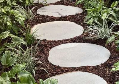 Concrete stepping stones in a garden path surrounded by plants and mulch