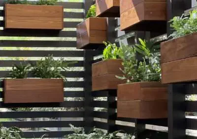 Wall-mounted wooden planter boxes filled with green plants on a black slatted wall.