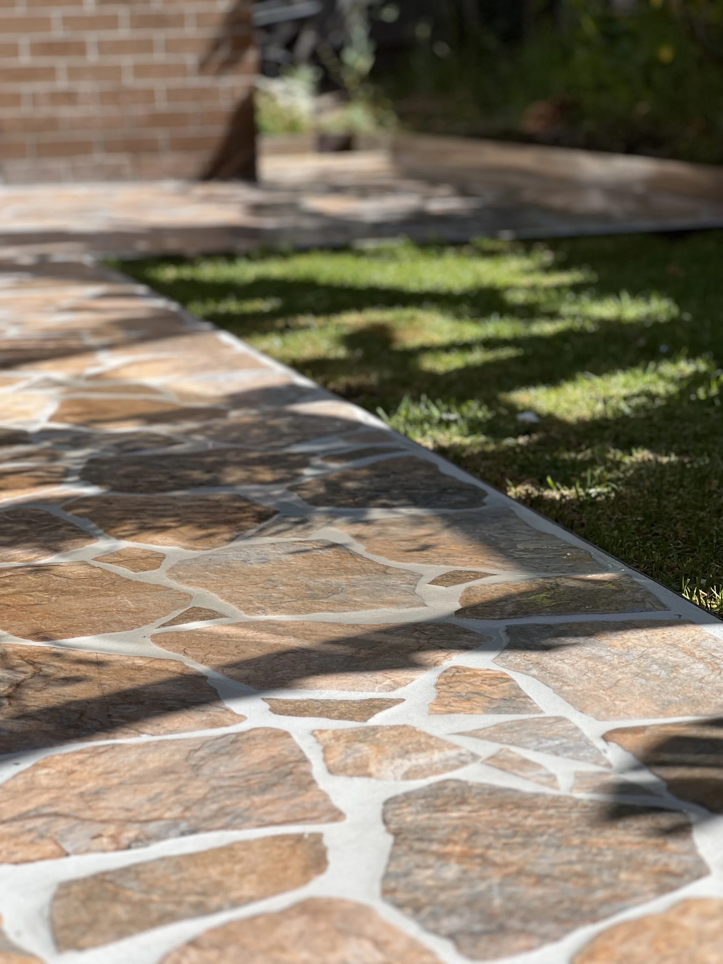 Close-up view of a stone walkway with irregularly shaped brown stones bordered by white mortar, casting shadows on the path.