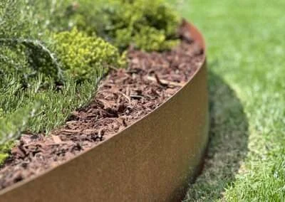 Close-up of a curved metal garden border with mulch and plants in a garden bed