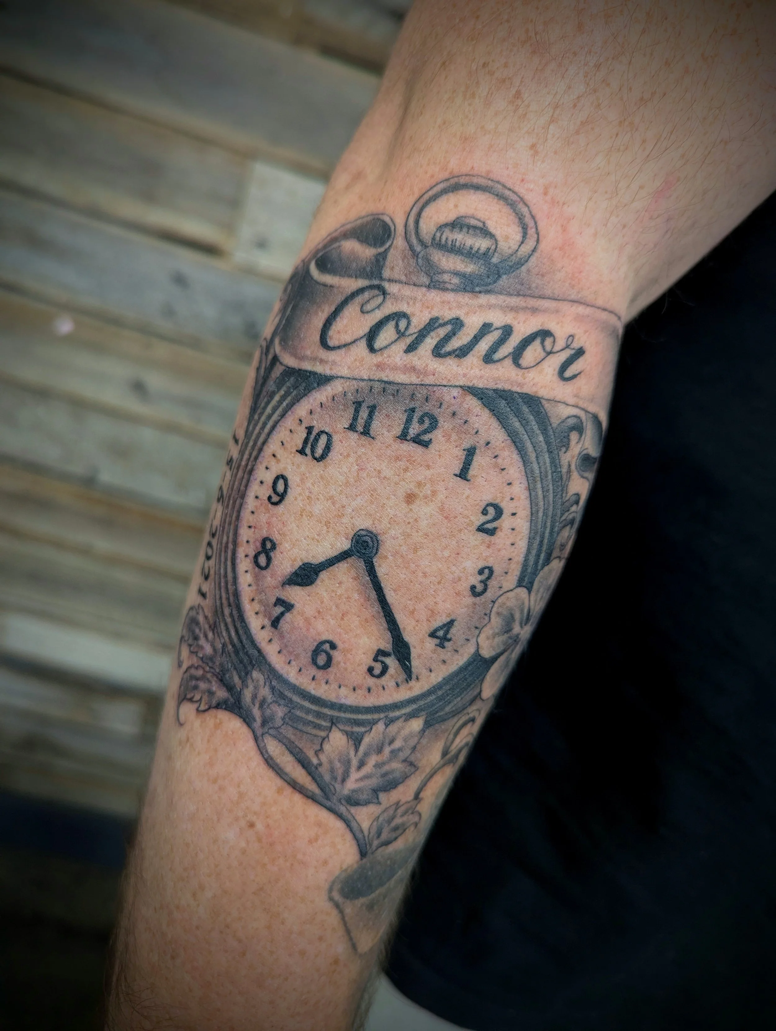 Tattoo of a vintage pocket watch with the word 'Conner' written above it on a person's arm.