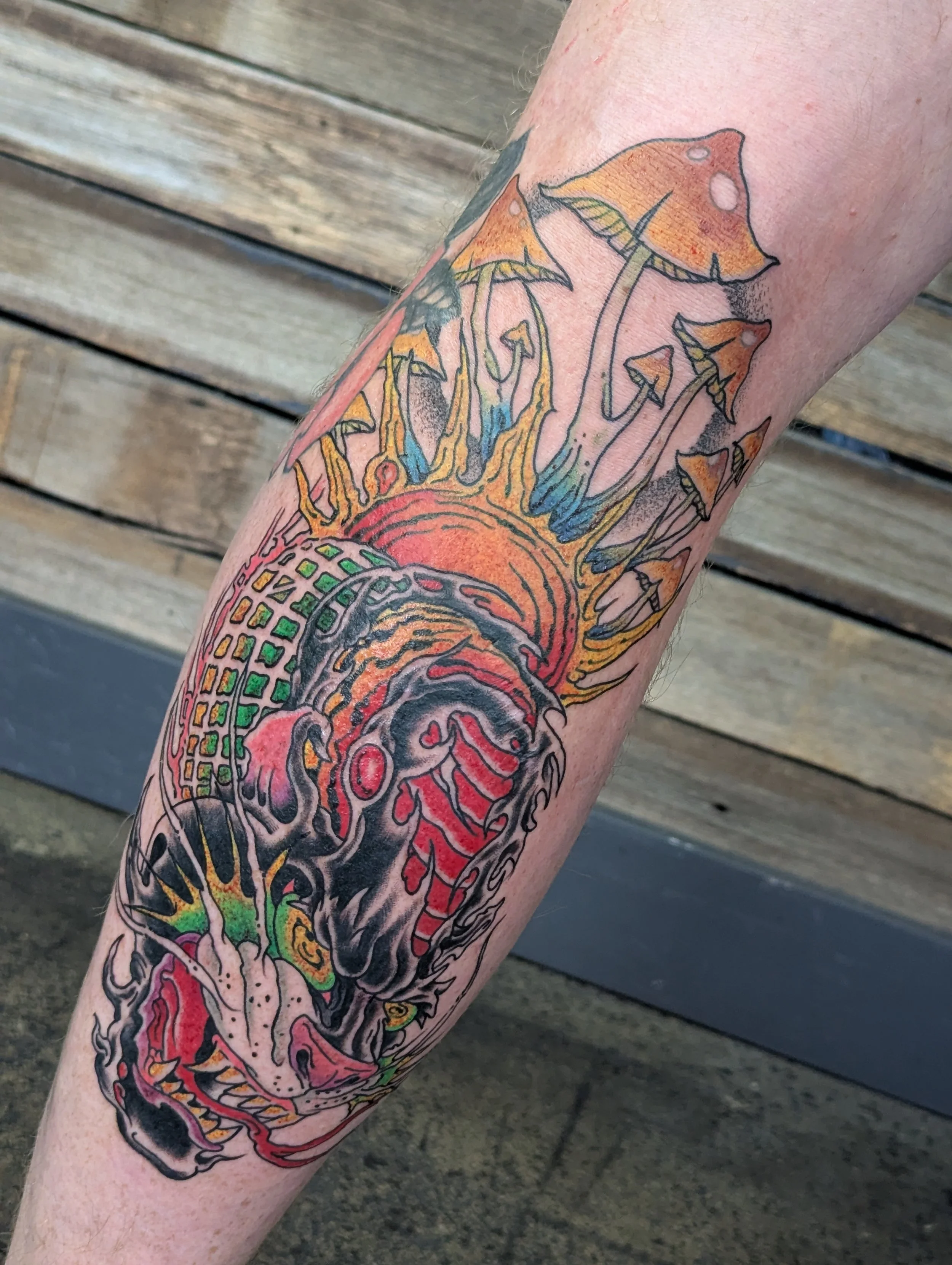 Colorful tattoo on a person's forearm, featuring mushrooms and abstract designs in shades of orange, pink, green, and black.