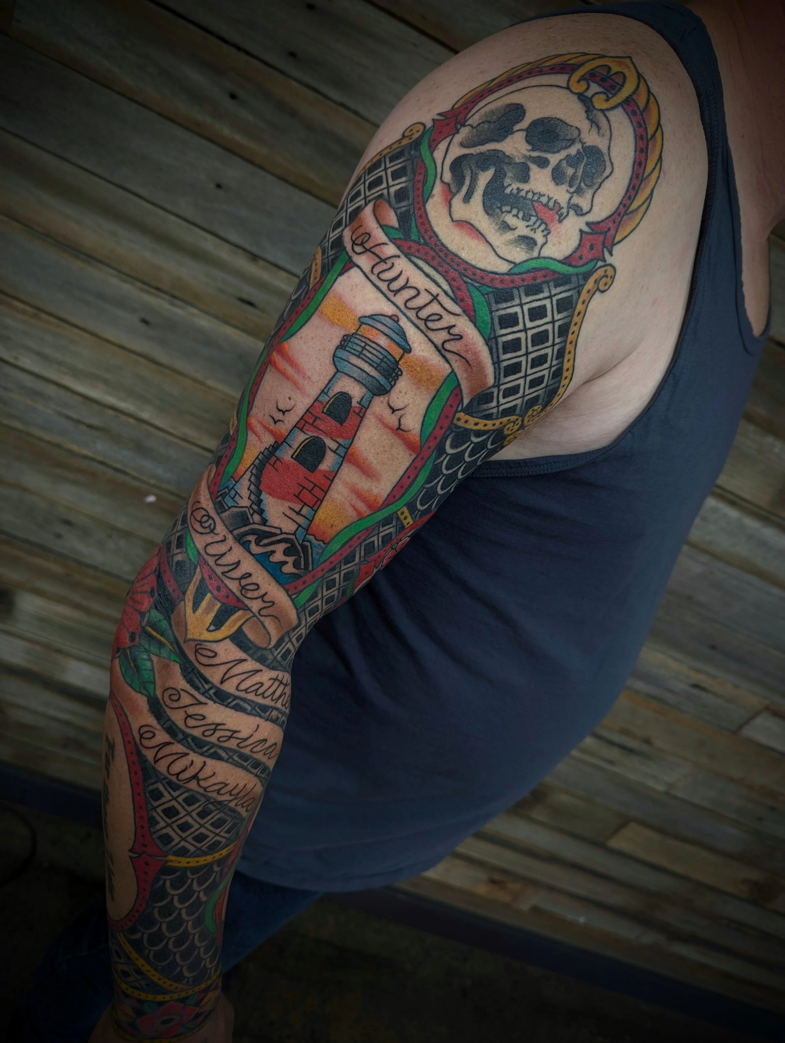 Colorful tattoo sleeve on a person's arm featuring a skull, lighthouse, and decorative elements, with the words 'Hunter' and 'Always' incorporated into the design.