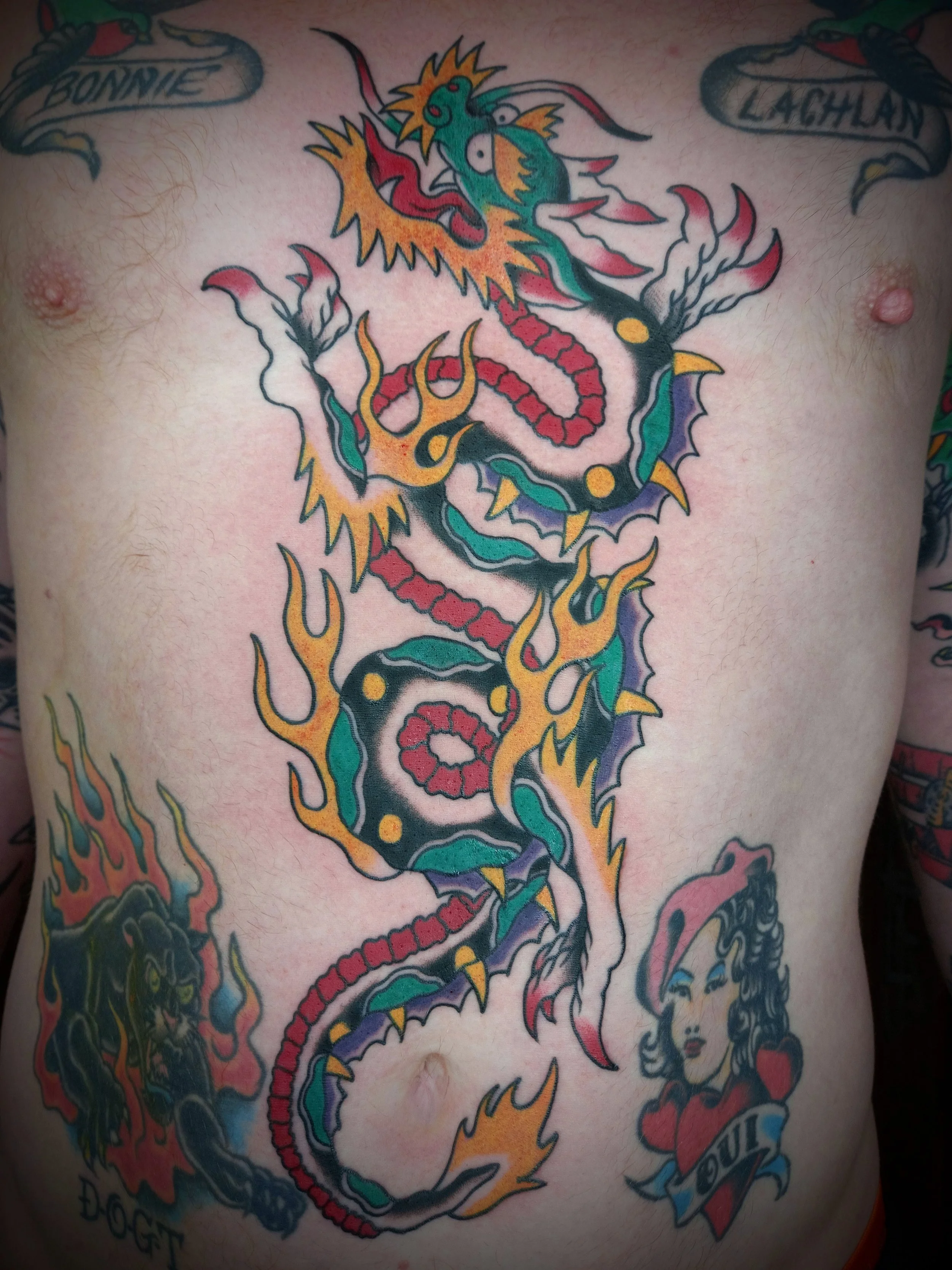 Colorful tattoo of a dragon on a person's chest, with banners and text.