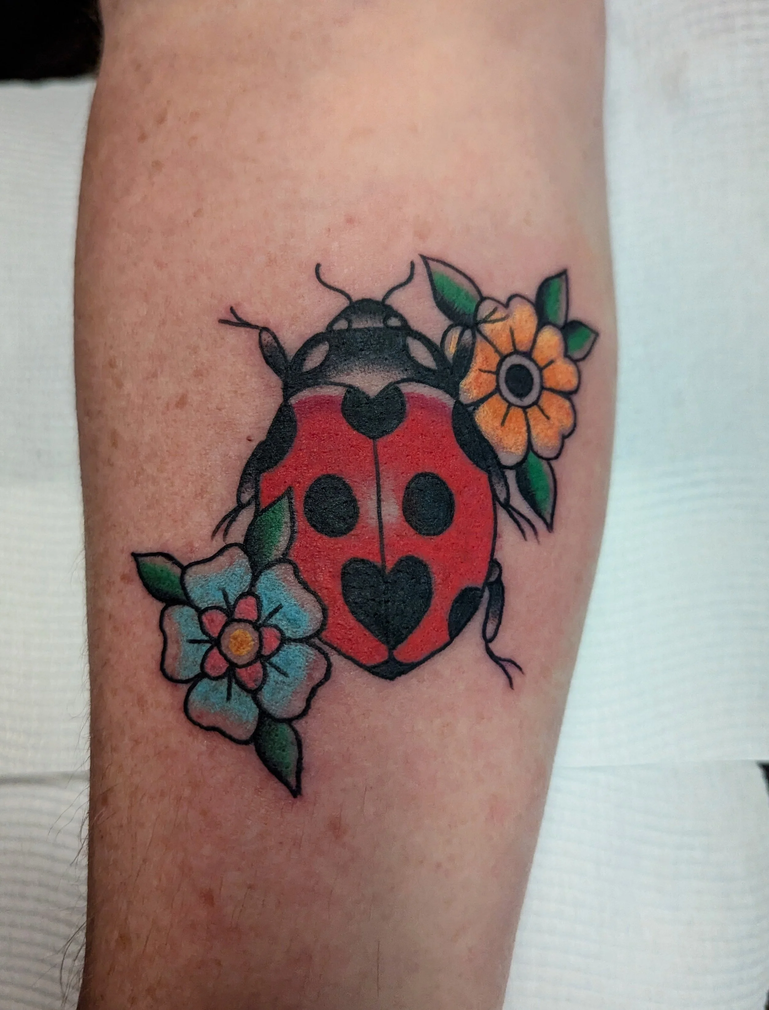 Colorful tattoo of a ladybug shape with flowers and leaves on skin.