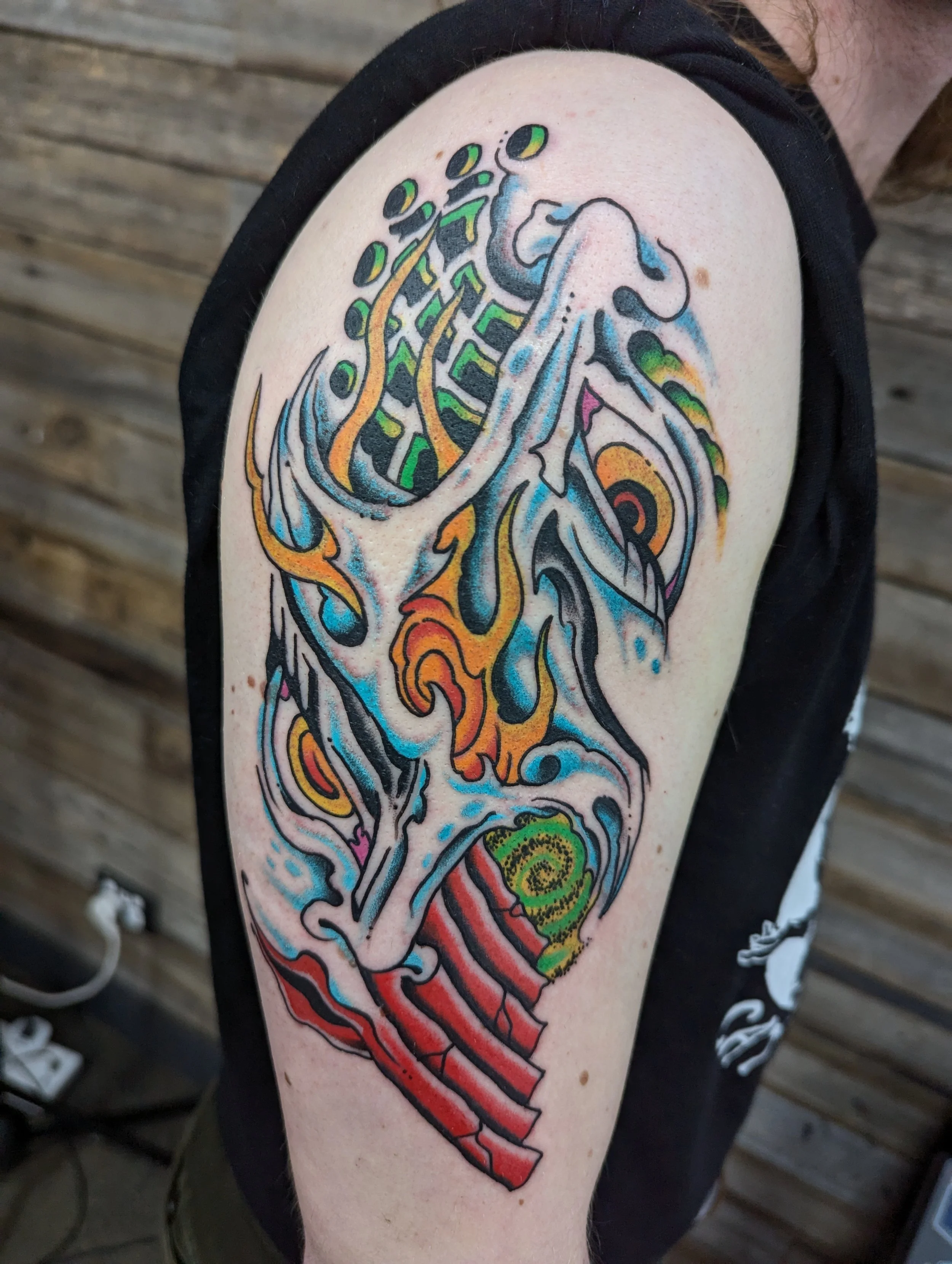 Colorful tattoo of a stylized whale with an abstract design on a person's upper arm, set against a background of wooden planks.