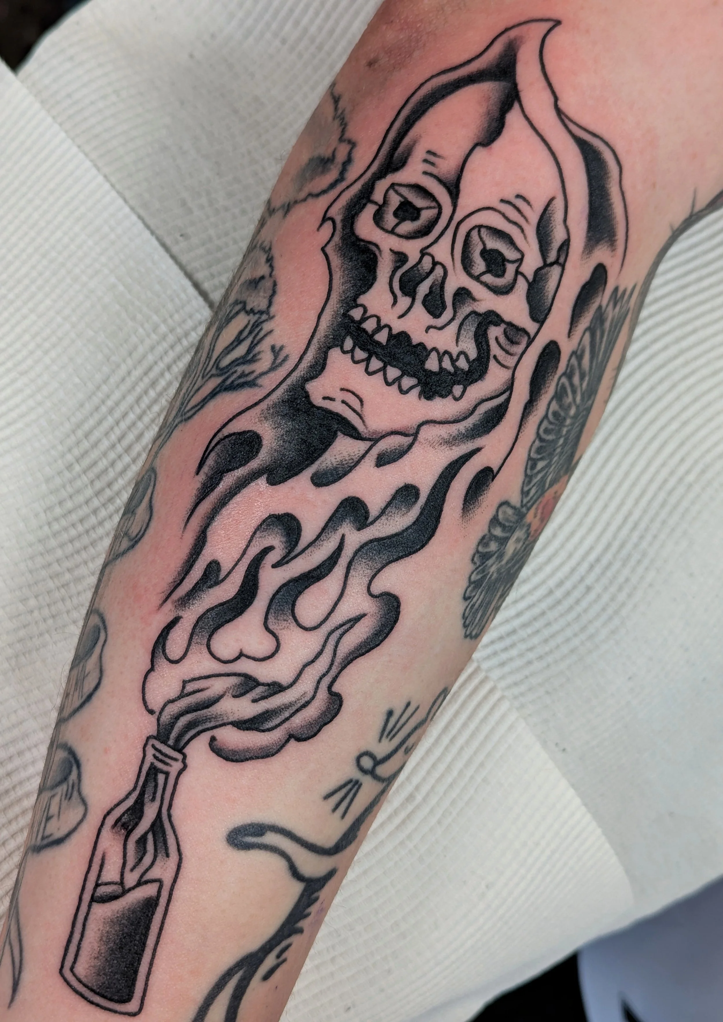 A tattoo of a human skull with a candle inside it on the arm, with flames and ink shading.