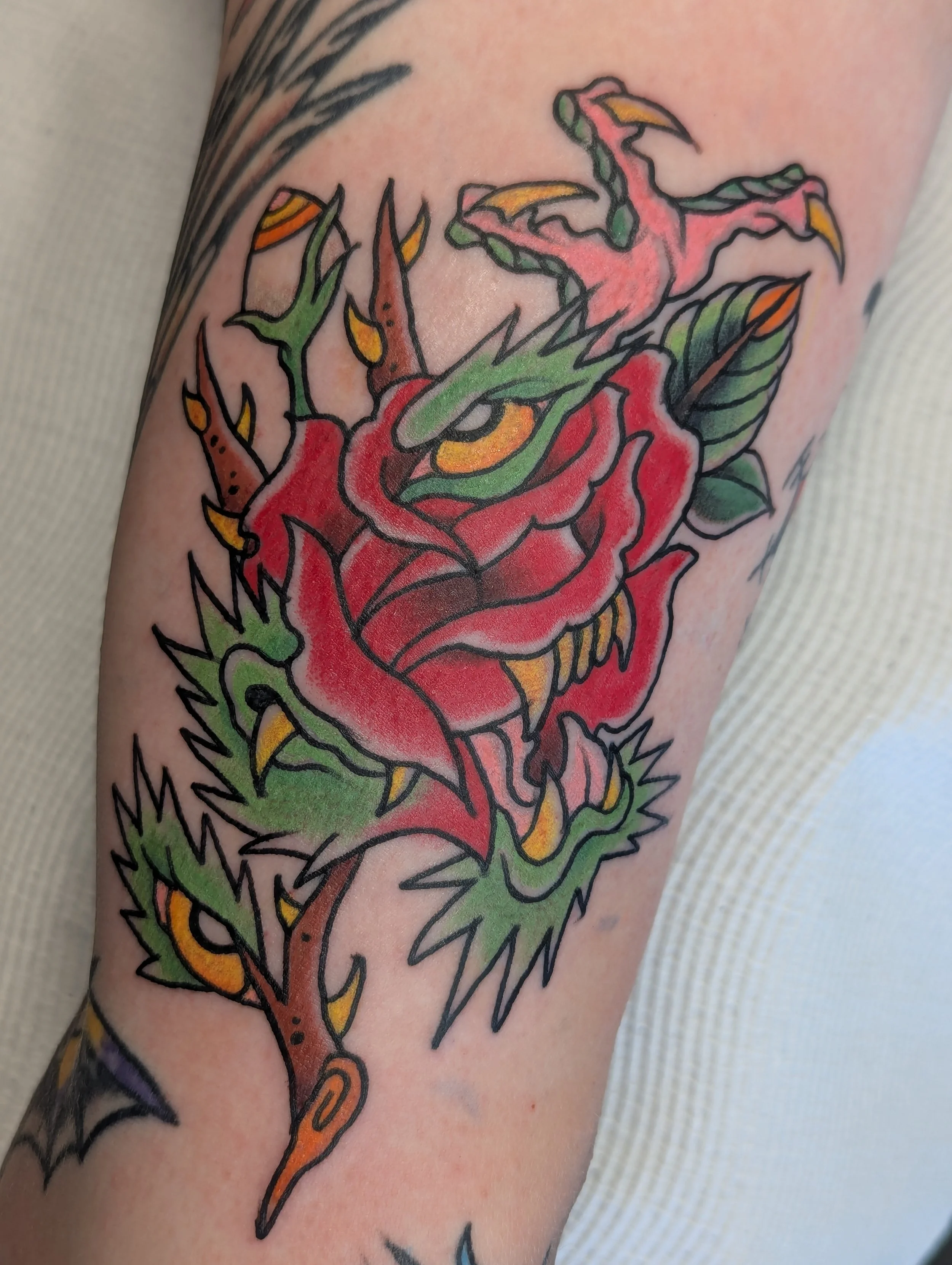 Colorful traditional-style tattoo of a dragon on person's arm, featuring a red body, green accents, yellow claws, and black outlines.