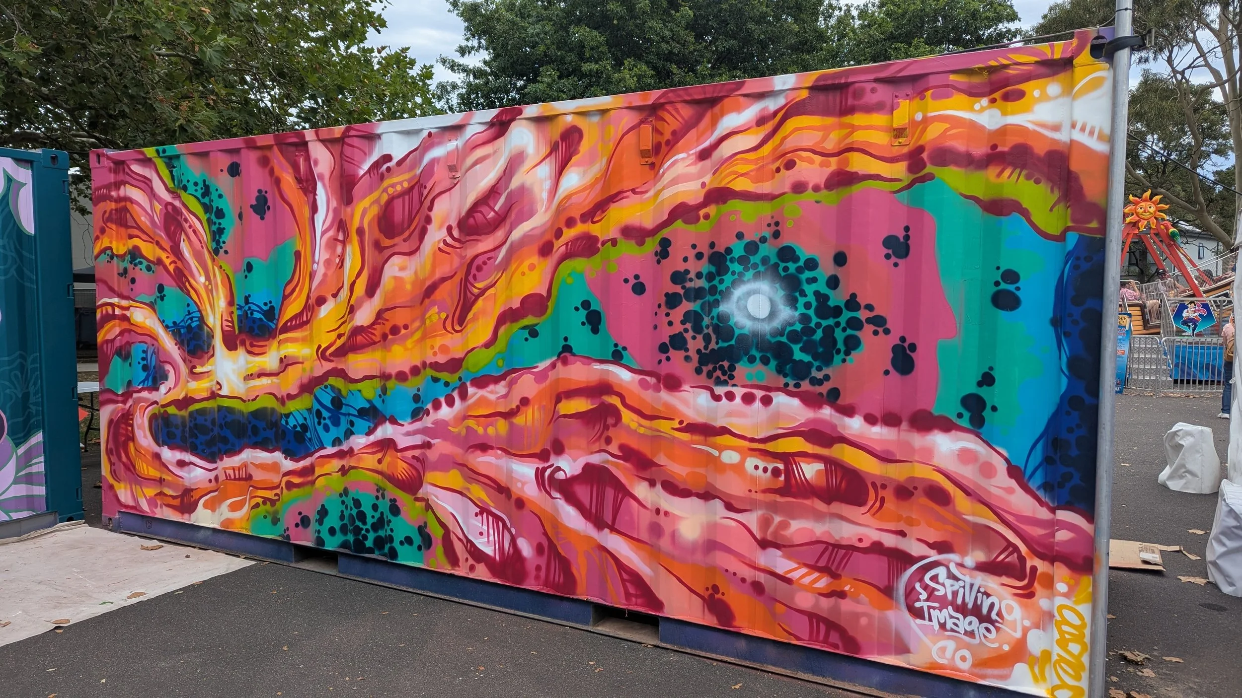Colorful abstract mural with swirling patterns in pink, orange, blue, green, and purple on a large outdoor wall.