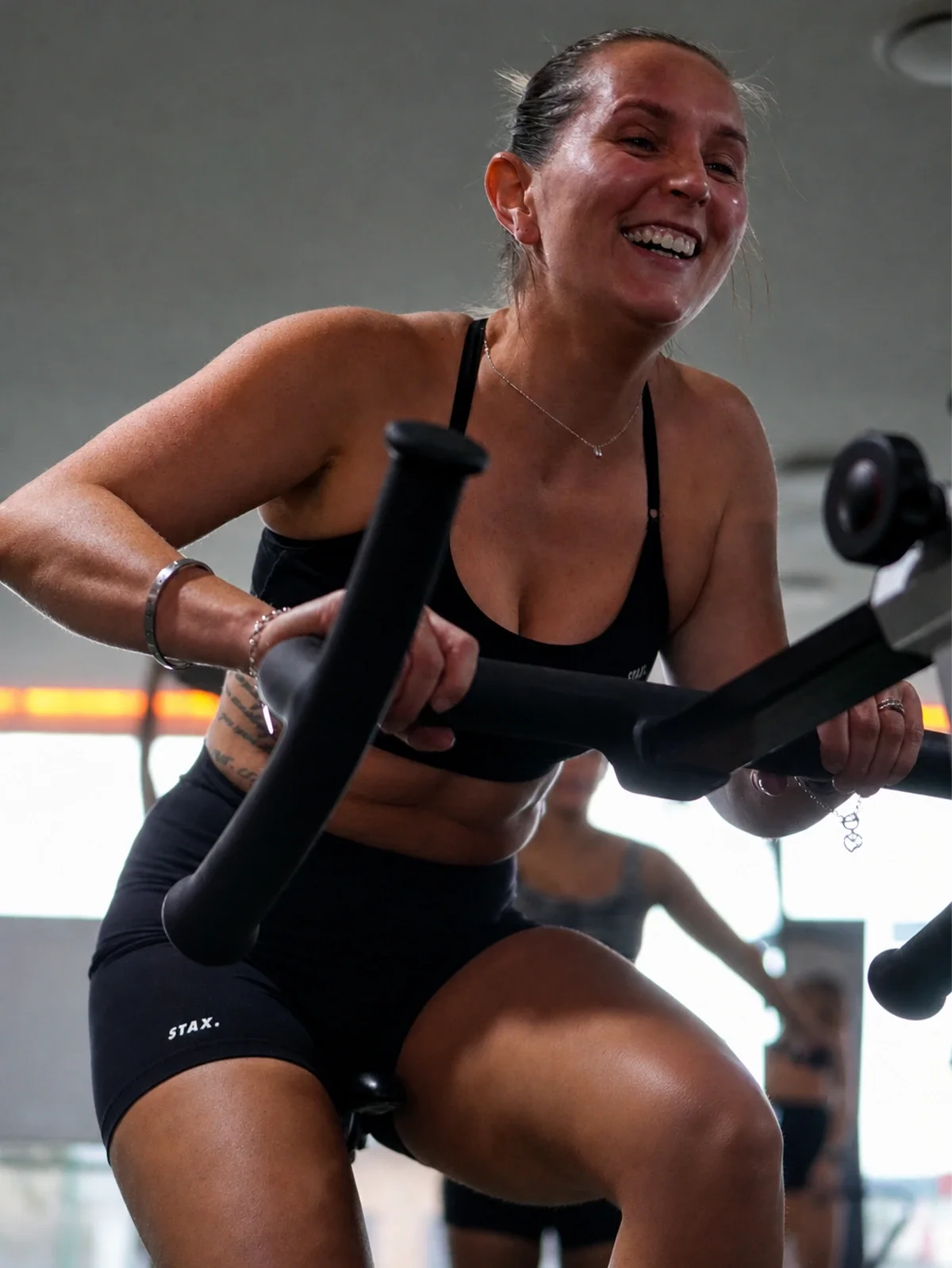 A woman smiling while working out on a rowing machine in a gym.