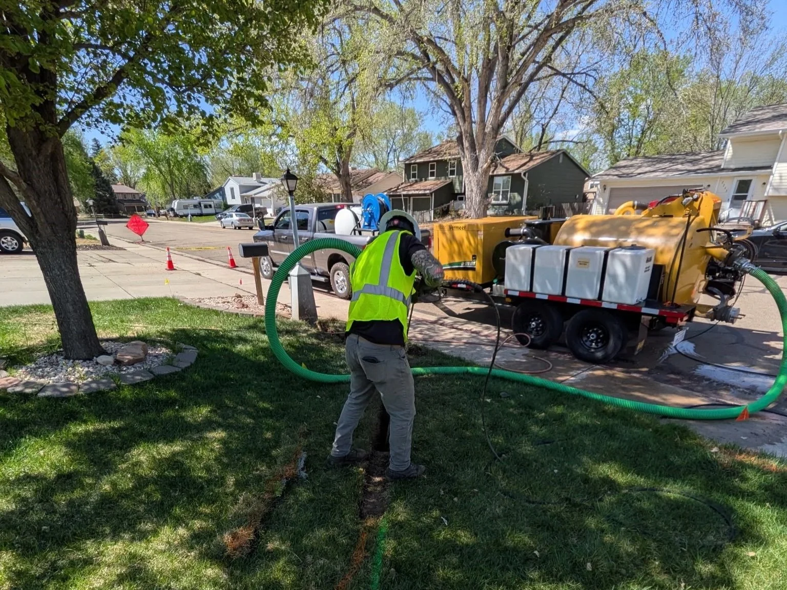 Worker in reflective vest operating a vacuum excavation machine on a lawn in a residential neighborhood. Fort Collins Loveland Windsor Greeley Estes Park Berthoud Longmont Johnstown Windsor Denver