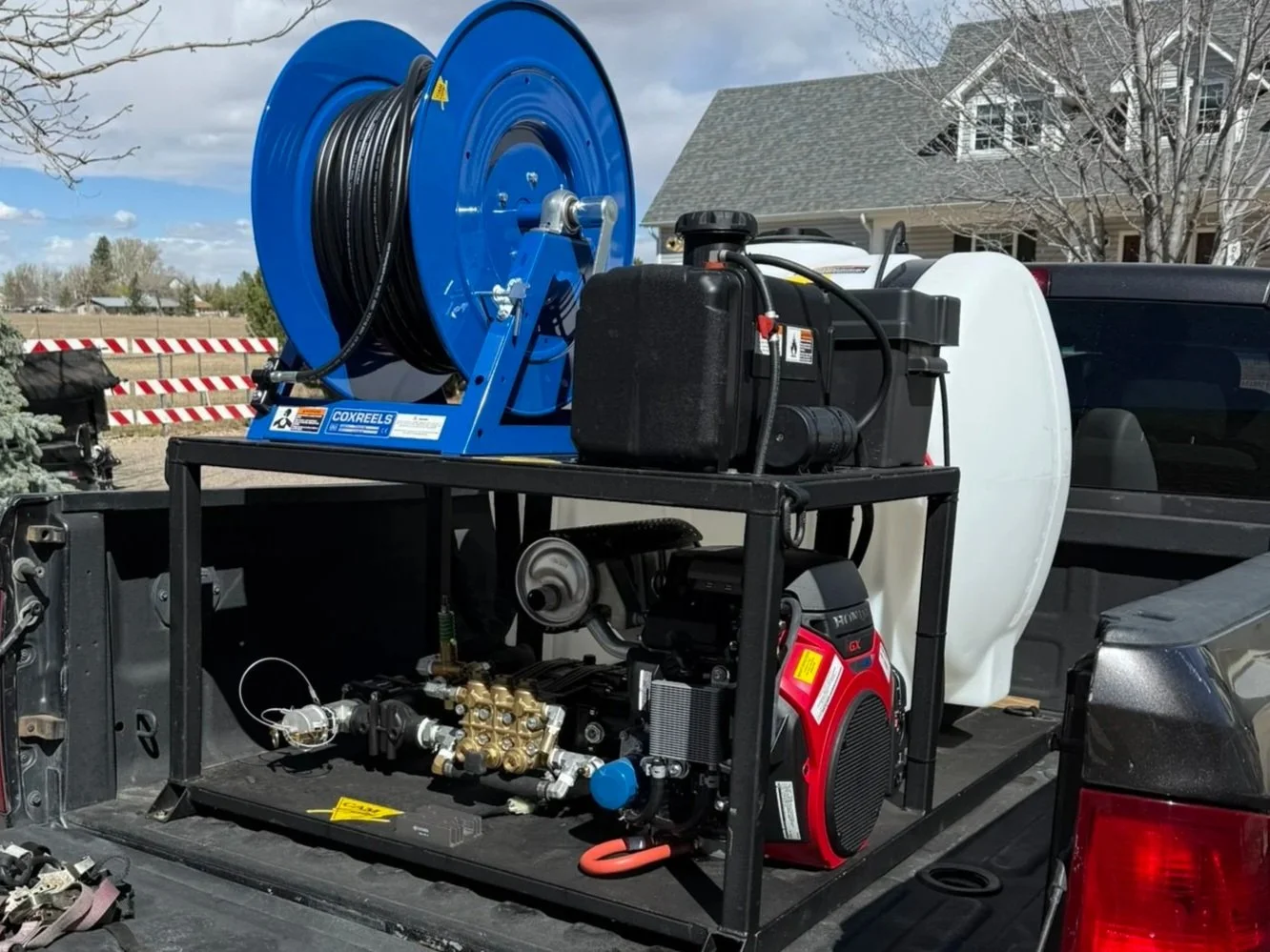 A hydro Jet Drain cleaning system mounted on a truck, featuring a large blue reel of hose, a white tank, and various hoses and fittings. Fort Collins Loveland Windsor Greeley Estes Park Berthoud Longmont Johnstown Windsor Denver