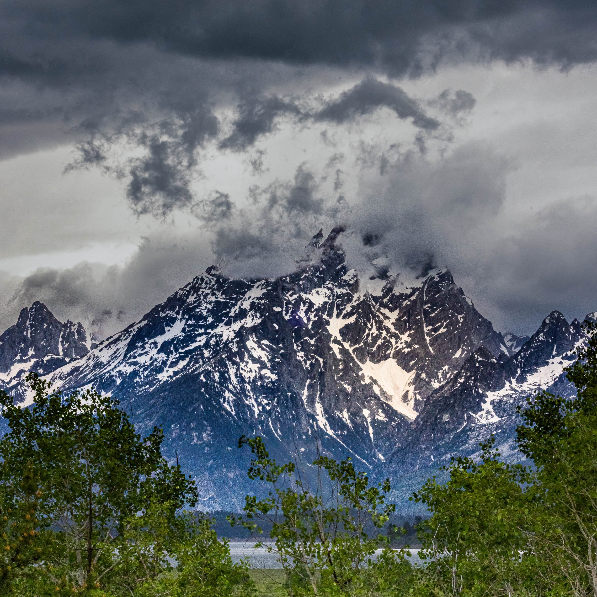  Teton Tempest 
Standing beneath the Tetons, I felt a profound sense of awe as the heavy storm clouds began to swallow the jagged peaks. It was incredible to watch nature completely hide such majestic beauty in a matter of minutes, leaving only hints