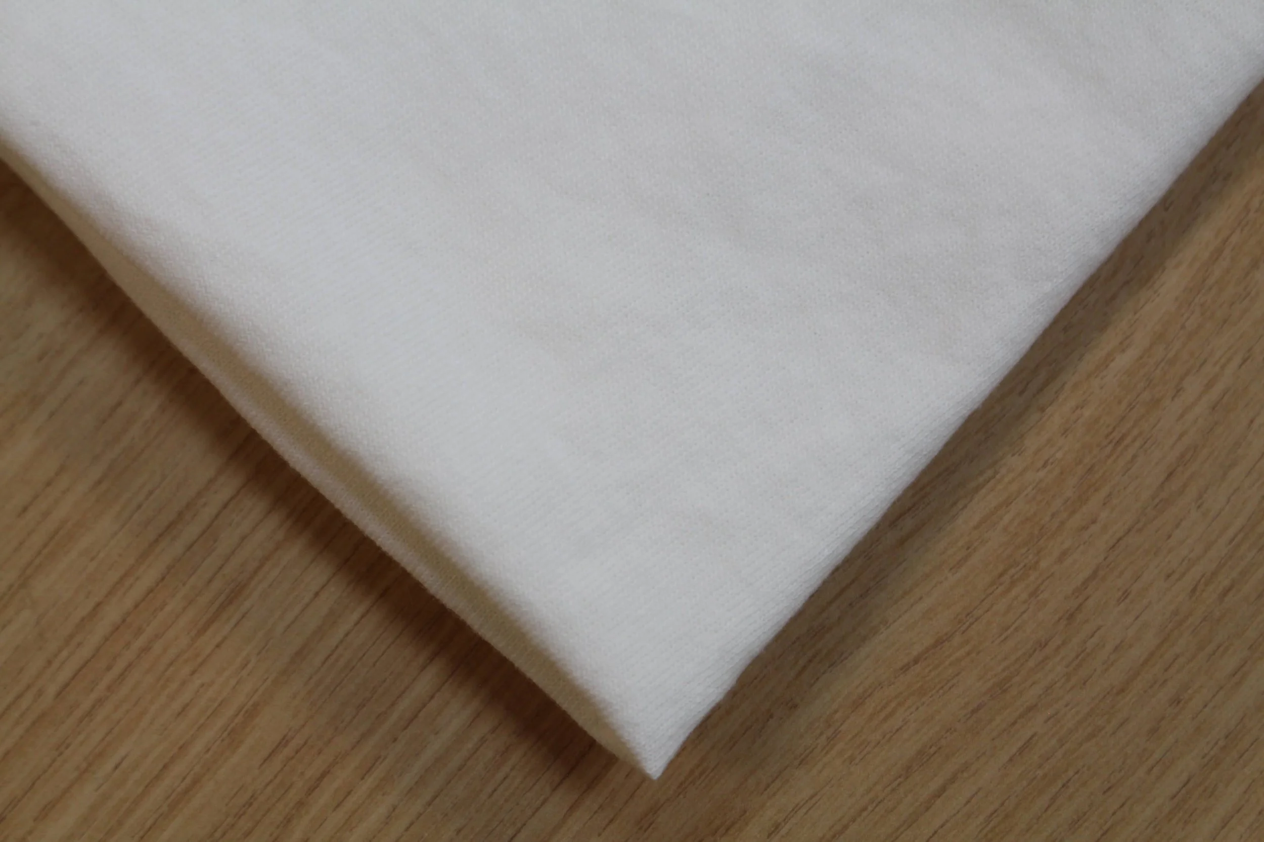 Close-up of a white, textured fabric with a smooth edge, resting on a wooden surface.
