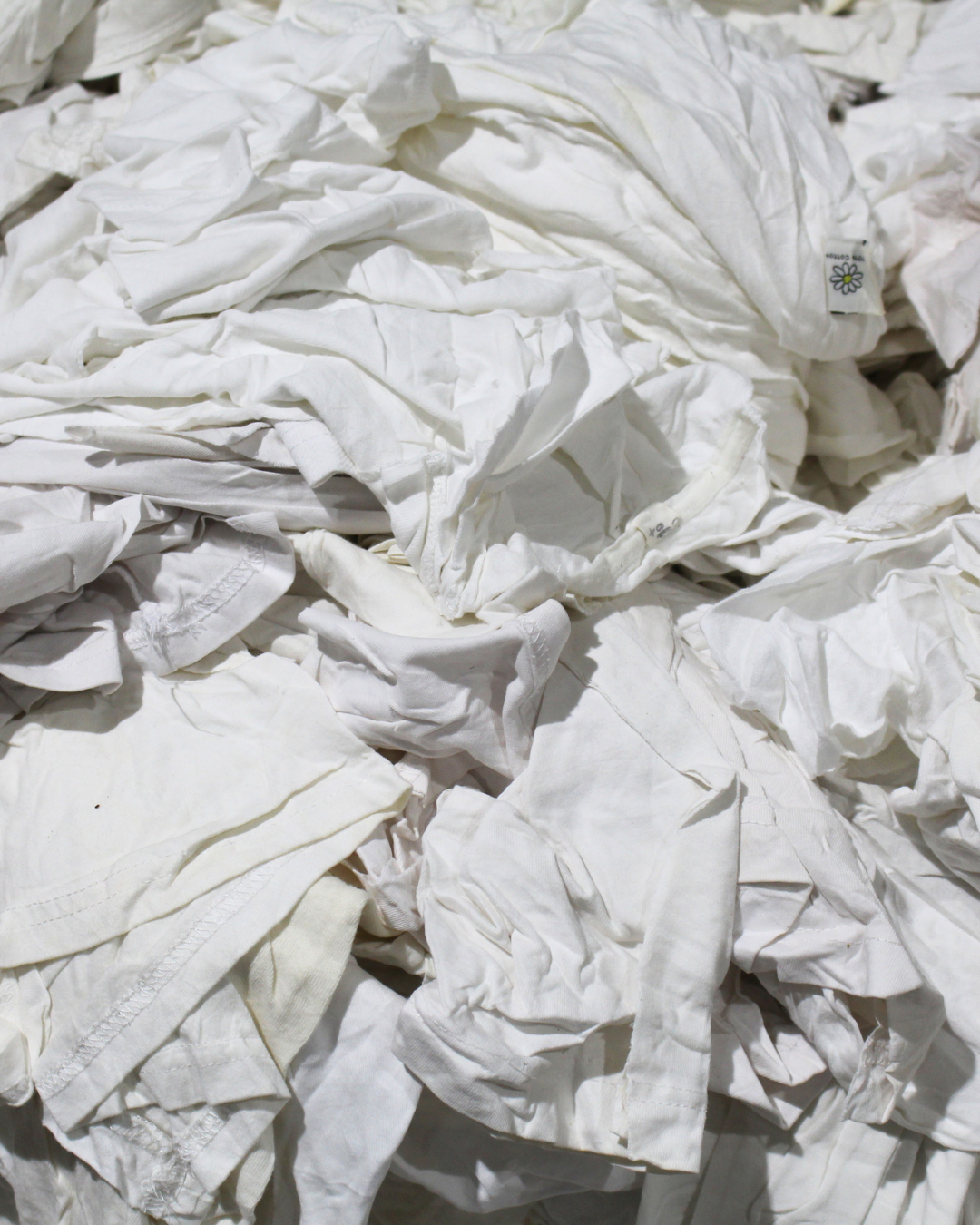 A pile of crumpled white fabric, disinfected and washed clothing or linens being cut into wash cloths.