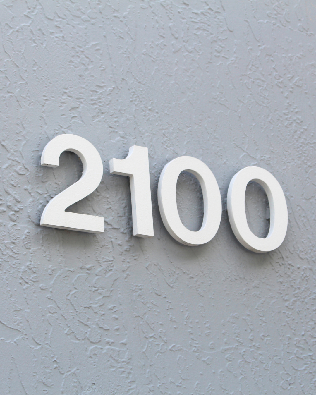 White 3D numbers reading 2100 mounted on a textured gray wall which is seen outside of the Troy Industries facility in Doral, Florida.