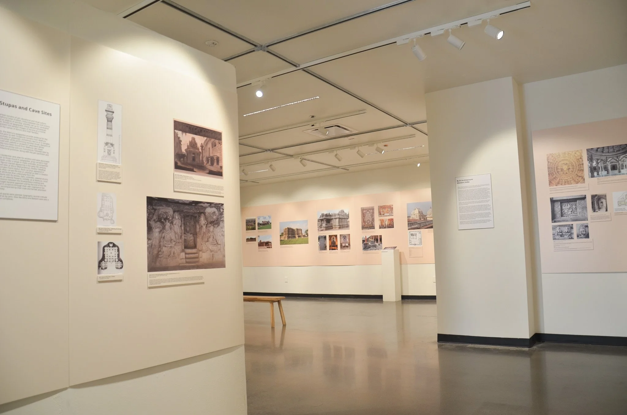 Interior of an art gallery or museum with white walls displaying photographs and informational plaques related to architecture, featuring a variety of structures and archaeological sites.