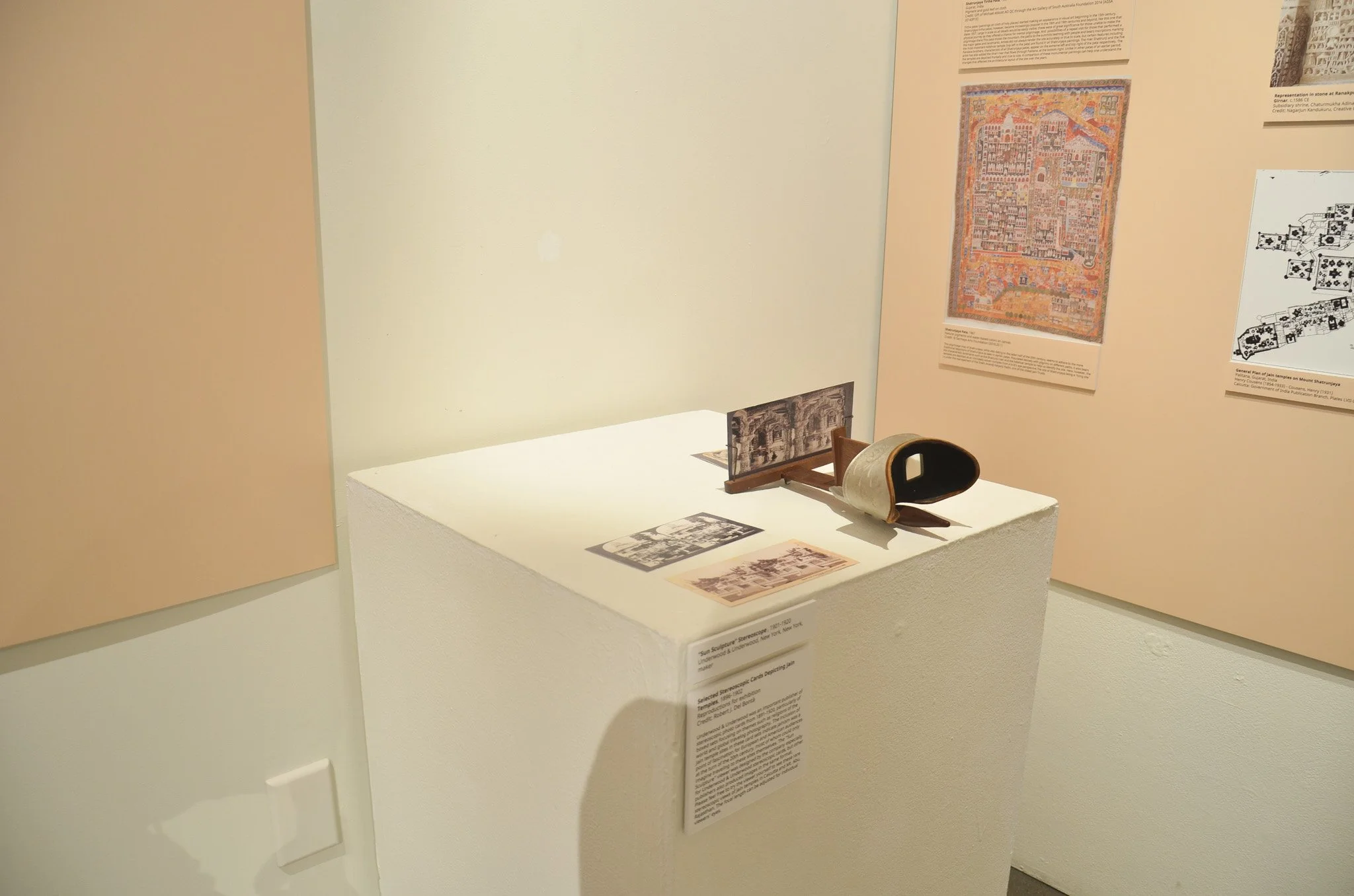Museum display with a roll of film on a stand, surrounded by photographs and informational panels. The background features large posters of artwork and text descriptions.