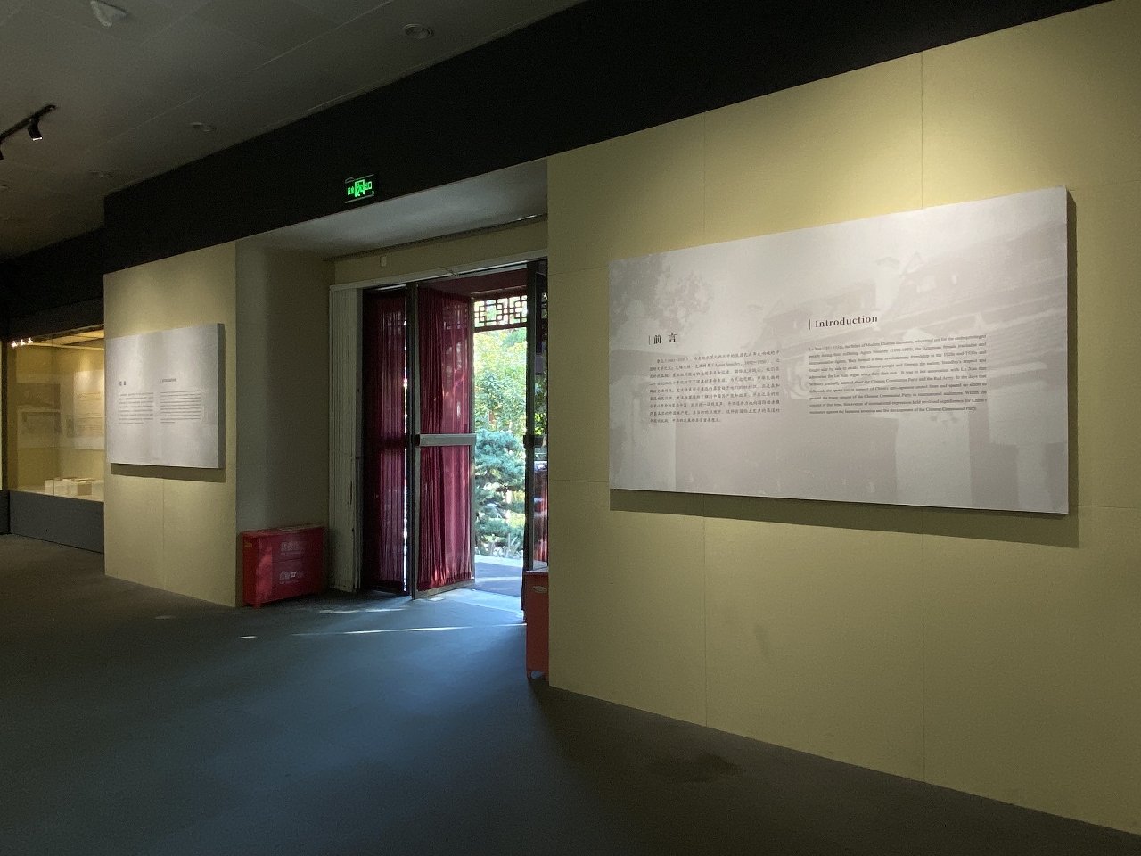 Museum interior with informational panels on the wall, an open door with red curtains, and a view of trees outside.