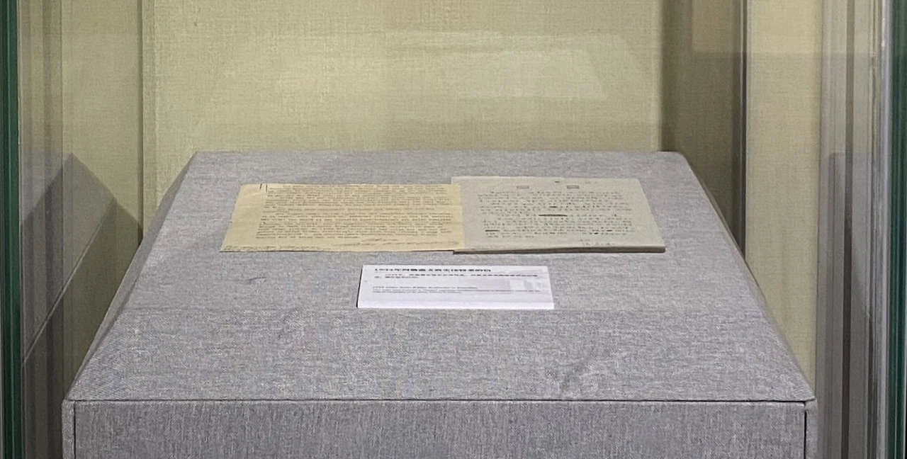Historical documents displayed inside a glass case on a gray fabric surface.