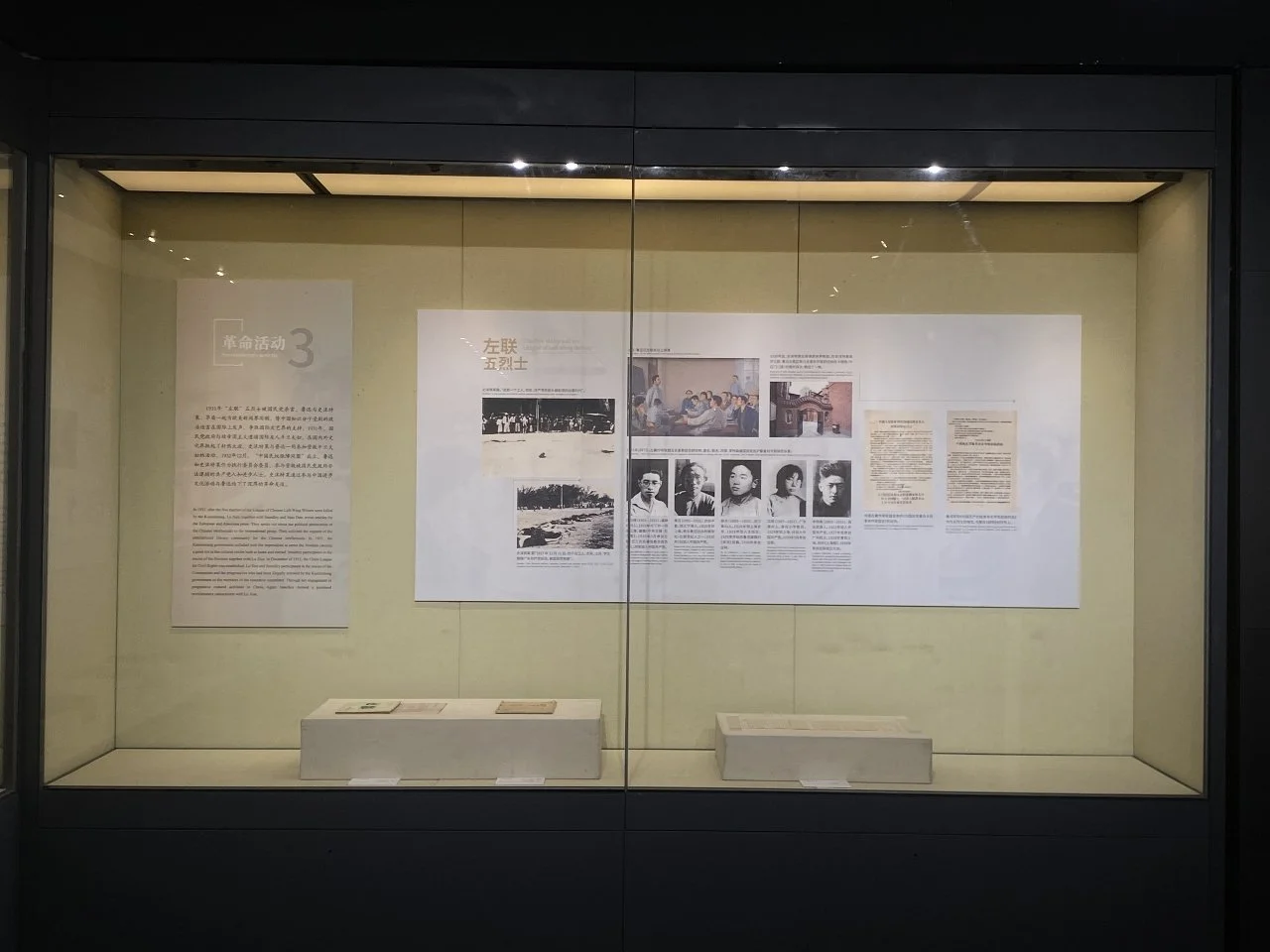 Museum display case with historical texts and black-and-white photographs on the wall behind.