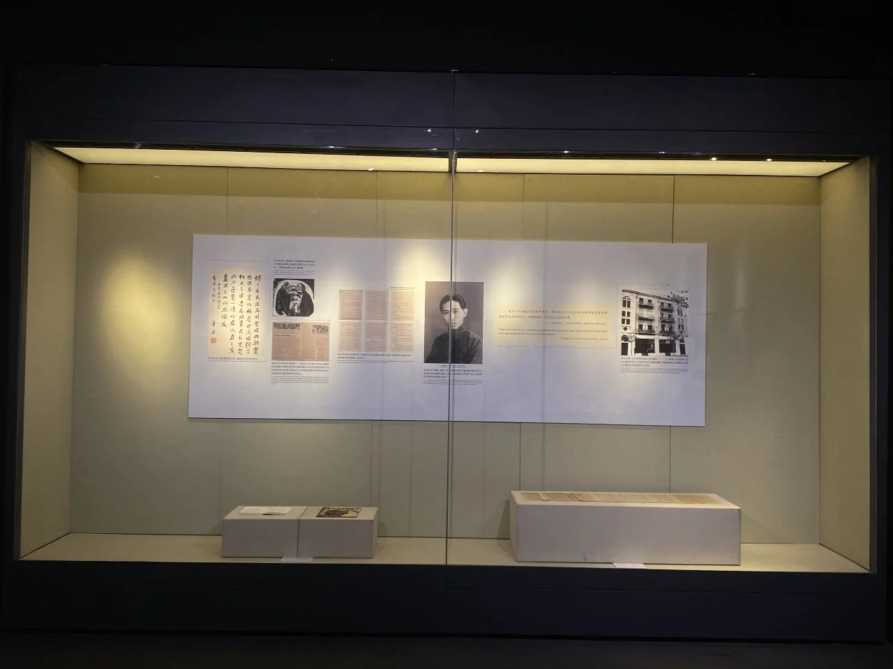 Display case with historical documents, photographs, and illustrations on a beige background.