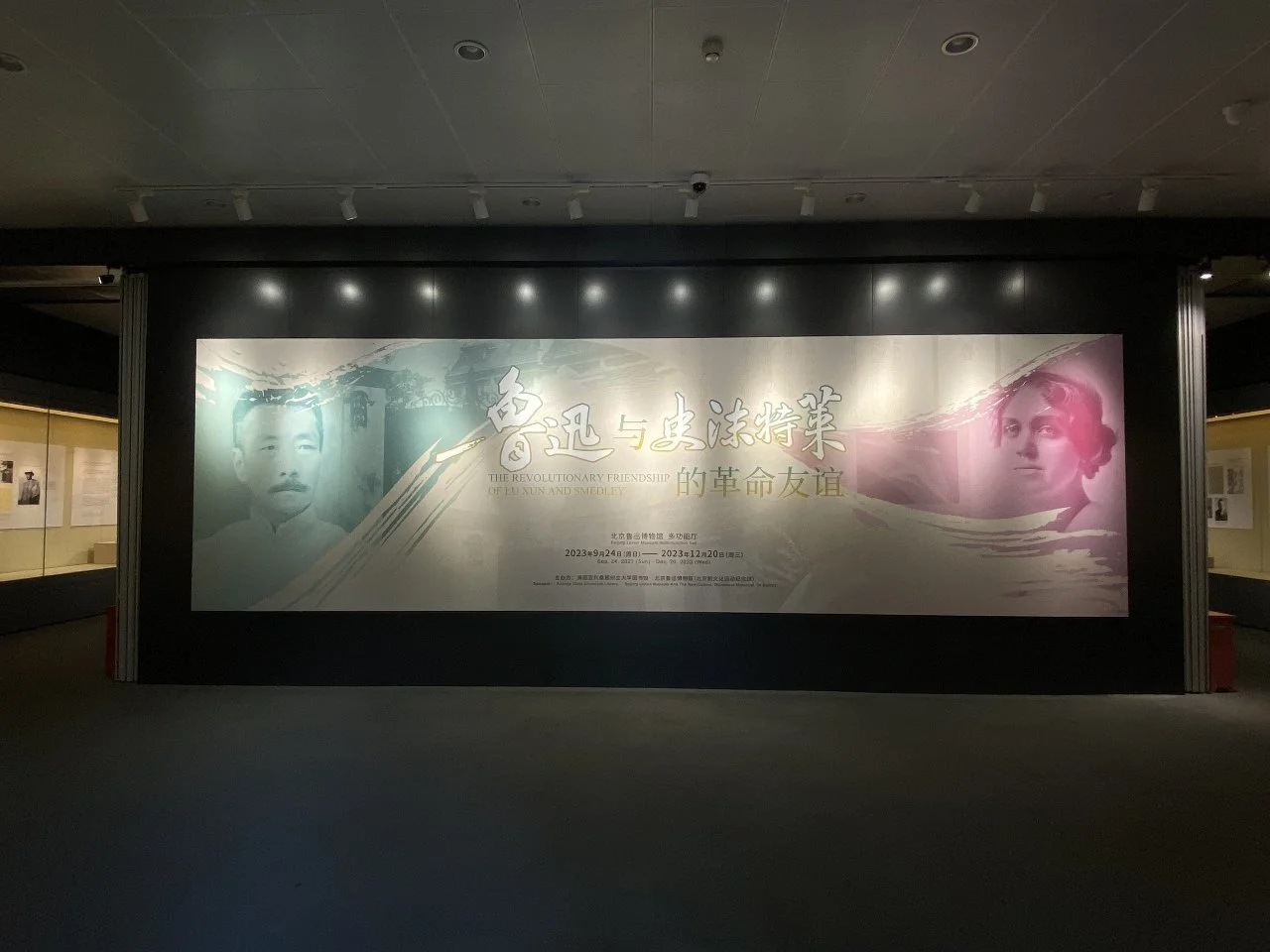 A large exhibition banner with Chinese and English text titled 'The Revolutionary Friendship of Lu Xun and Smedley' displayed in a museum setting; features faded images of Lu Xun, a Chinese writer, and a woman on the right.