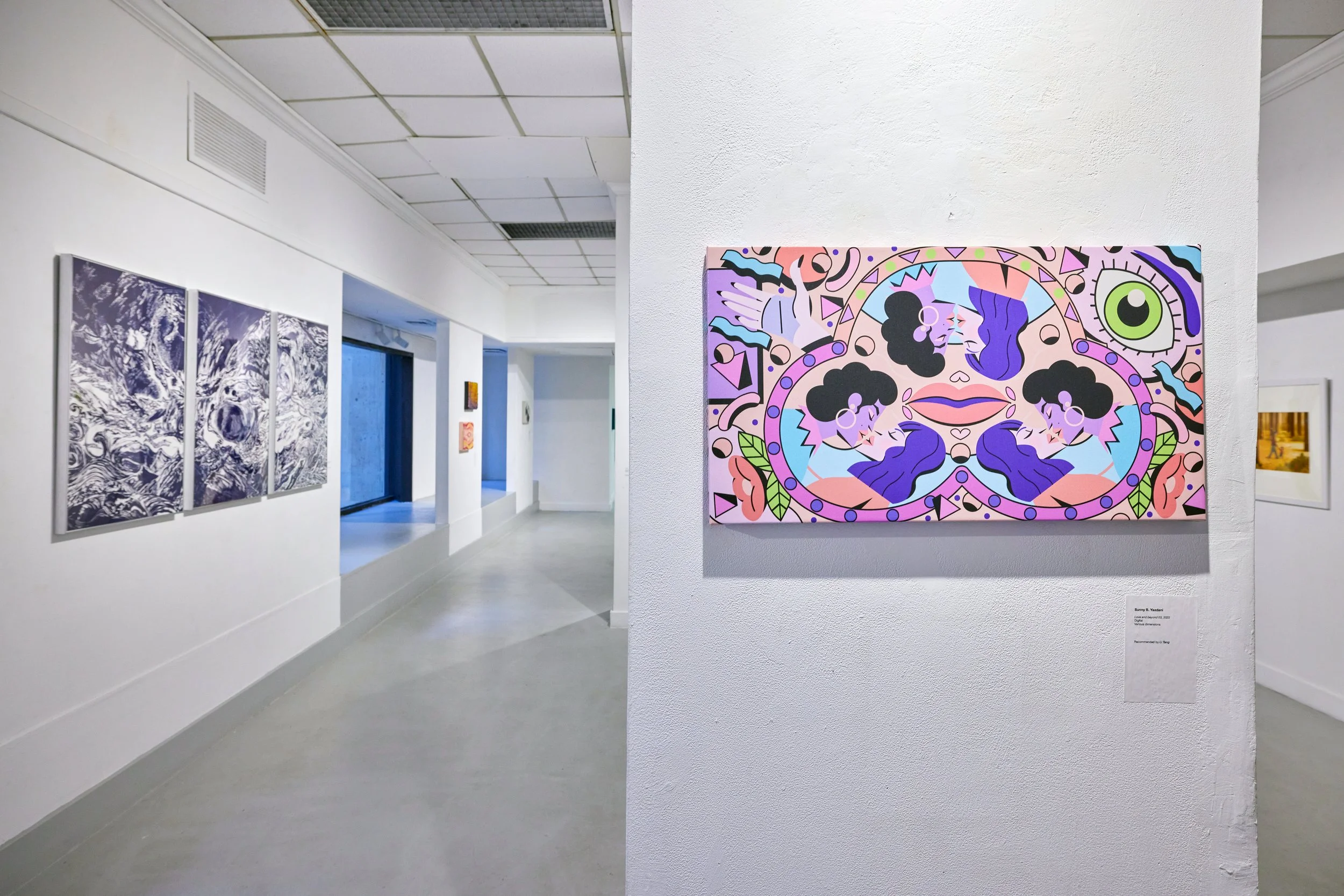 An art gallery with white walls and ceiling, displaying a colorful abstract painting on the right and black-and-white ocean wave artwork on the left. The gallery has a large window and a clean, minimalist design.