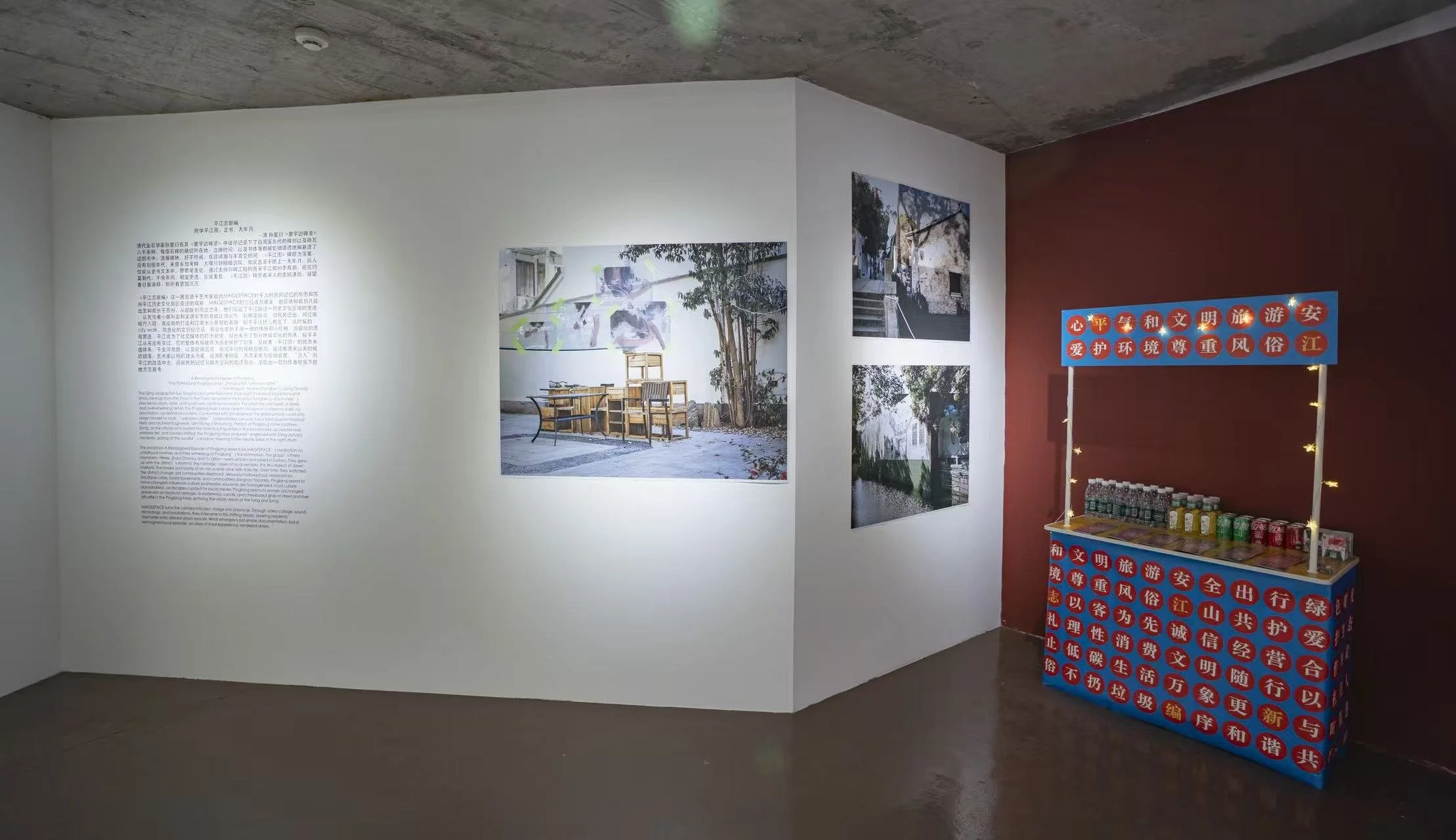 Exhibition wall with text and several landscape photographs, next to a red wall with a stand of bottled drinks and snacks in Chinese characters.