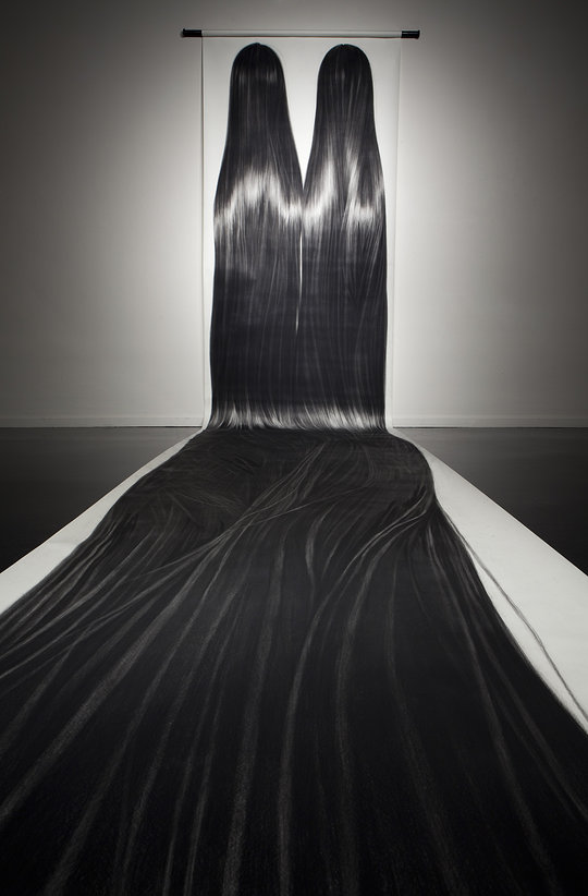 An art installation resembling a tree with black and white streaks, with a long, flowing fabric extending from the base to the top, hanging in a gallery setting.
