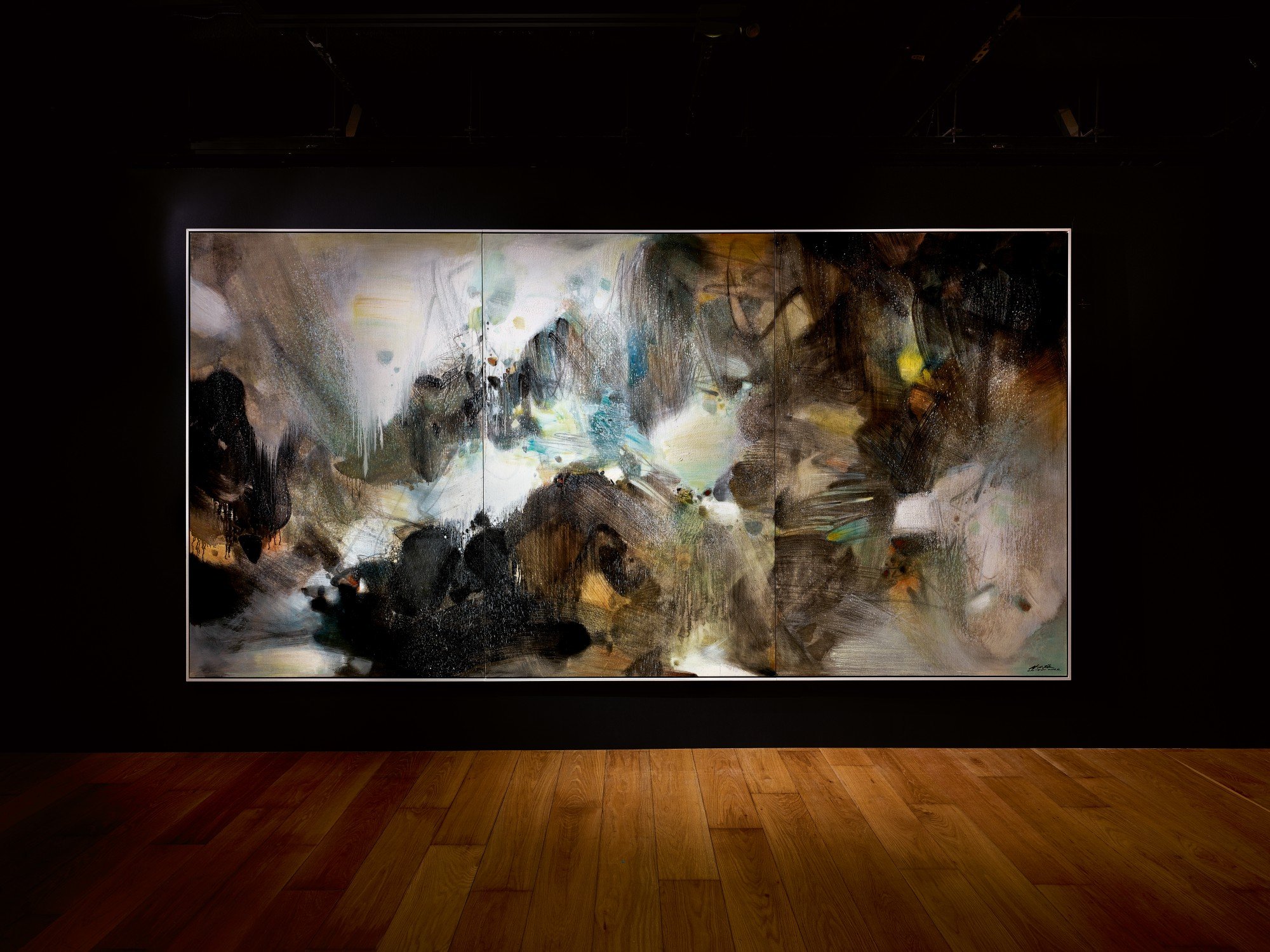 Large abstract painting with dark and light colors, black, brown, and hints of blue and yellow, displayed on a wall in an art gallery or museum.