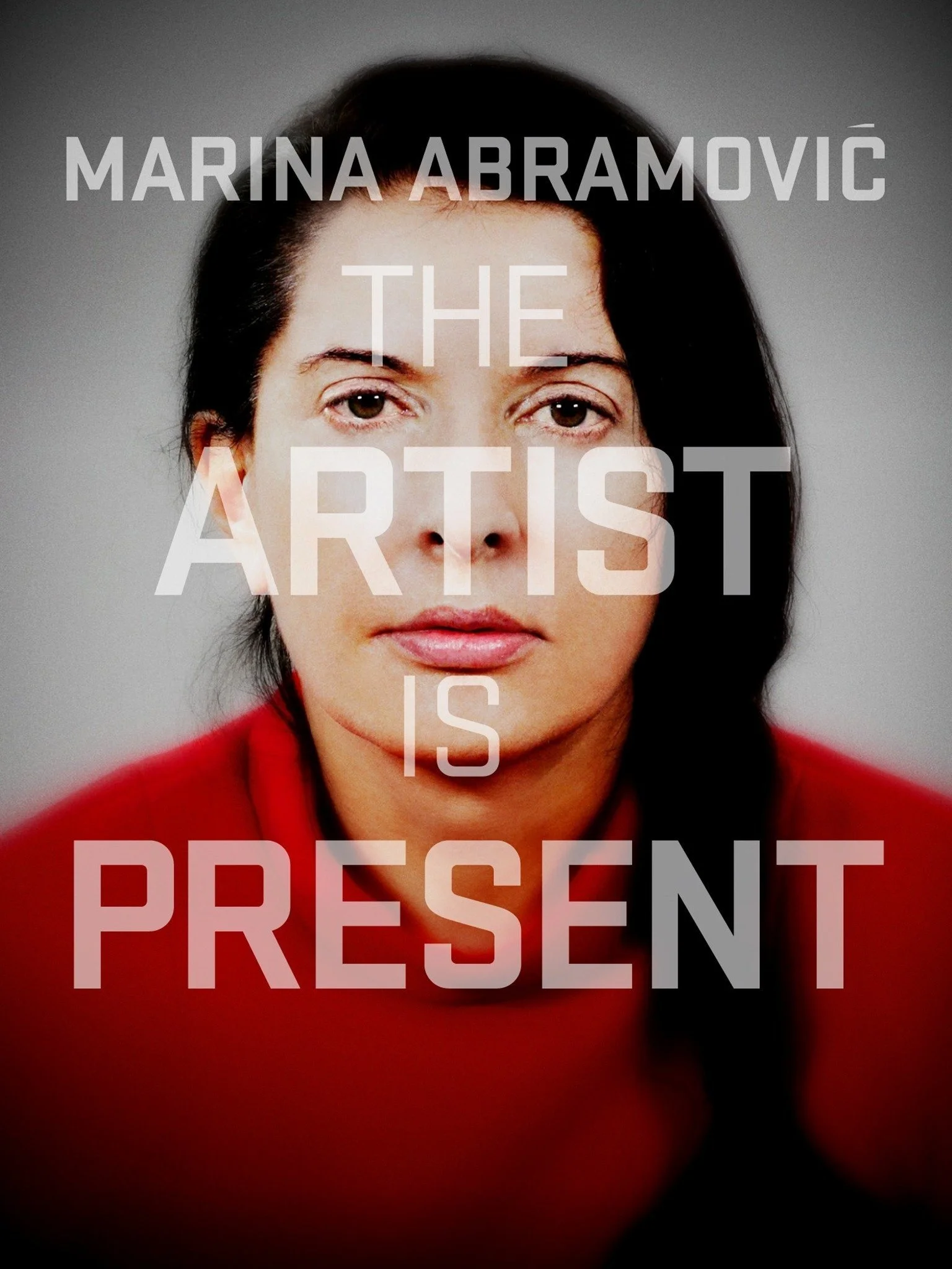Close-up portrait of a woman with dark hair and a serious expression, wearing a red top, with overlaid text reading "Marina Abramović - The Artist is Present."