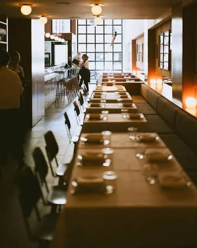 Empty restaurant dining area with neatly arranged tables, chairs, and dim lighting, featuring a large window at the back.