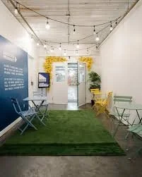 A cozy indoor space with string lights, a green rug, outdoor chairs, and a yellow flower decoration on the wall.
