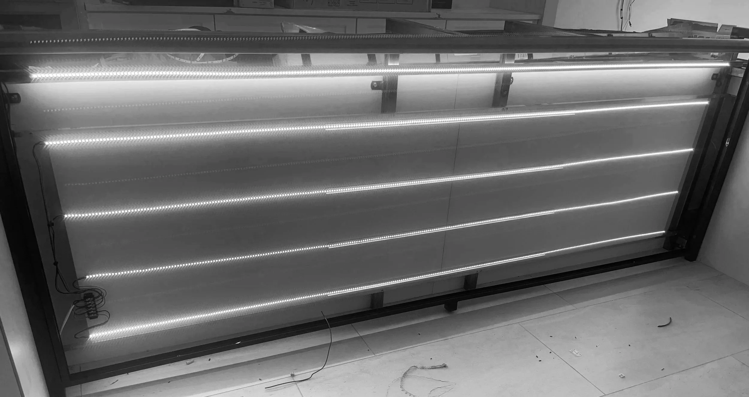 Unlit LED display panel with horizontal rows of small lights, partially assembled and leaning against a wall, with some wires and components visible.