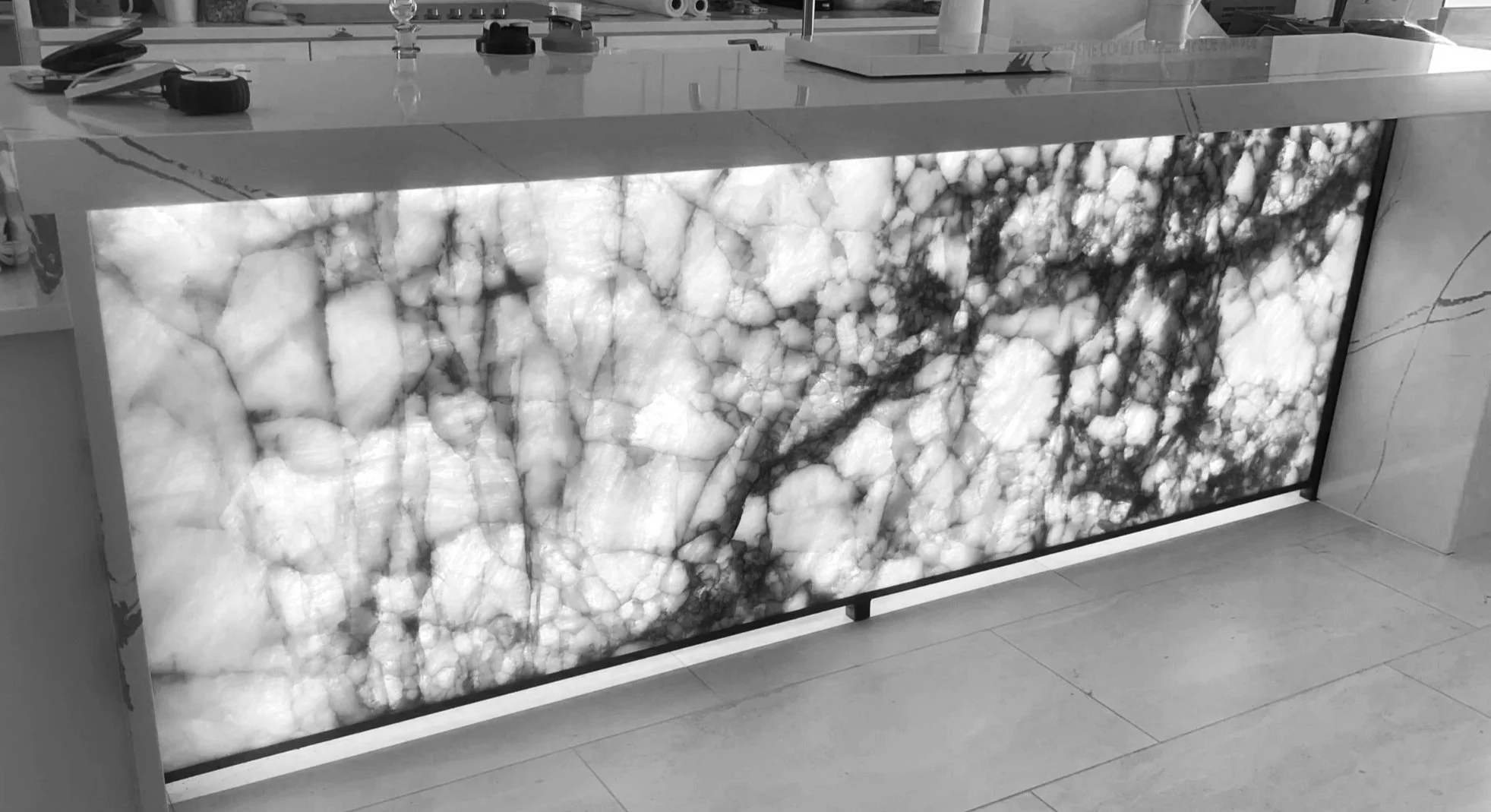 A backlit onyx marble wall panel with white and gray veining, mounted on a wall in an indoor setting.