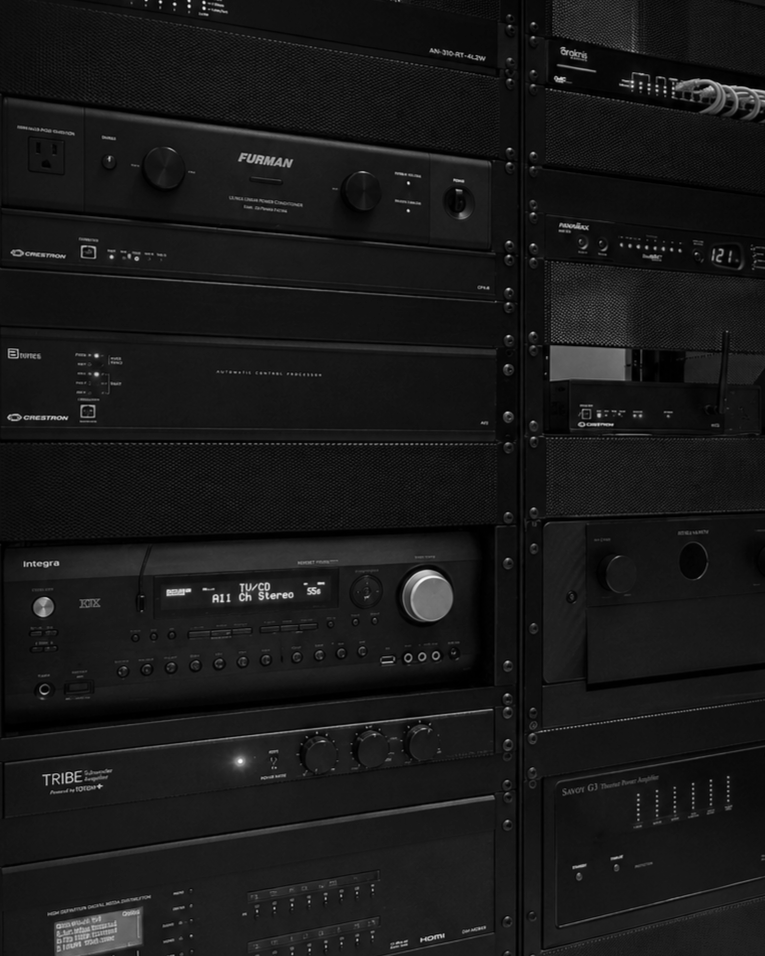 A black and white photo of several audio and video equipment rack units stacked vertically, including amplifiers, receivers, and controllers.