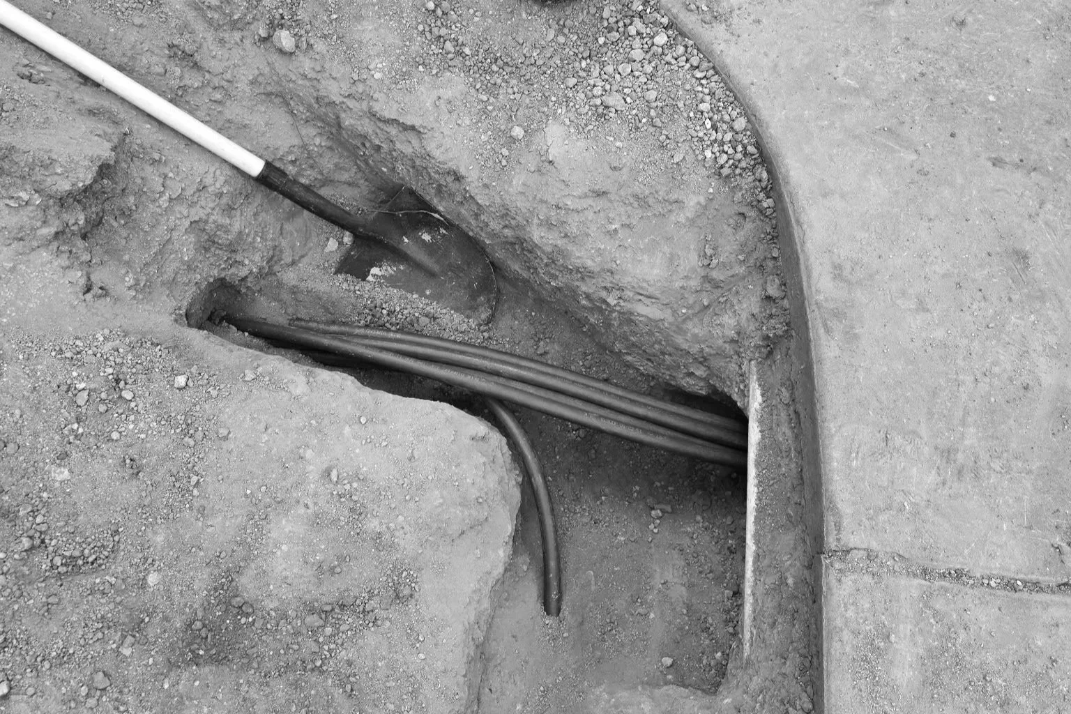 Underground utility box with cables and a shovel in a dirt excavation site.