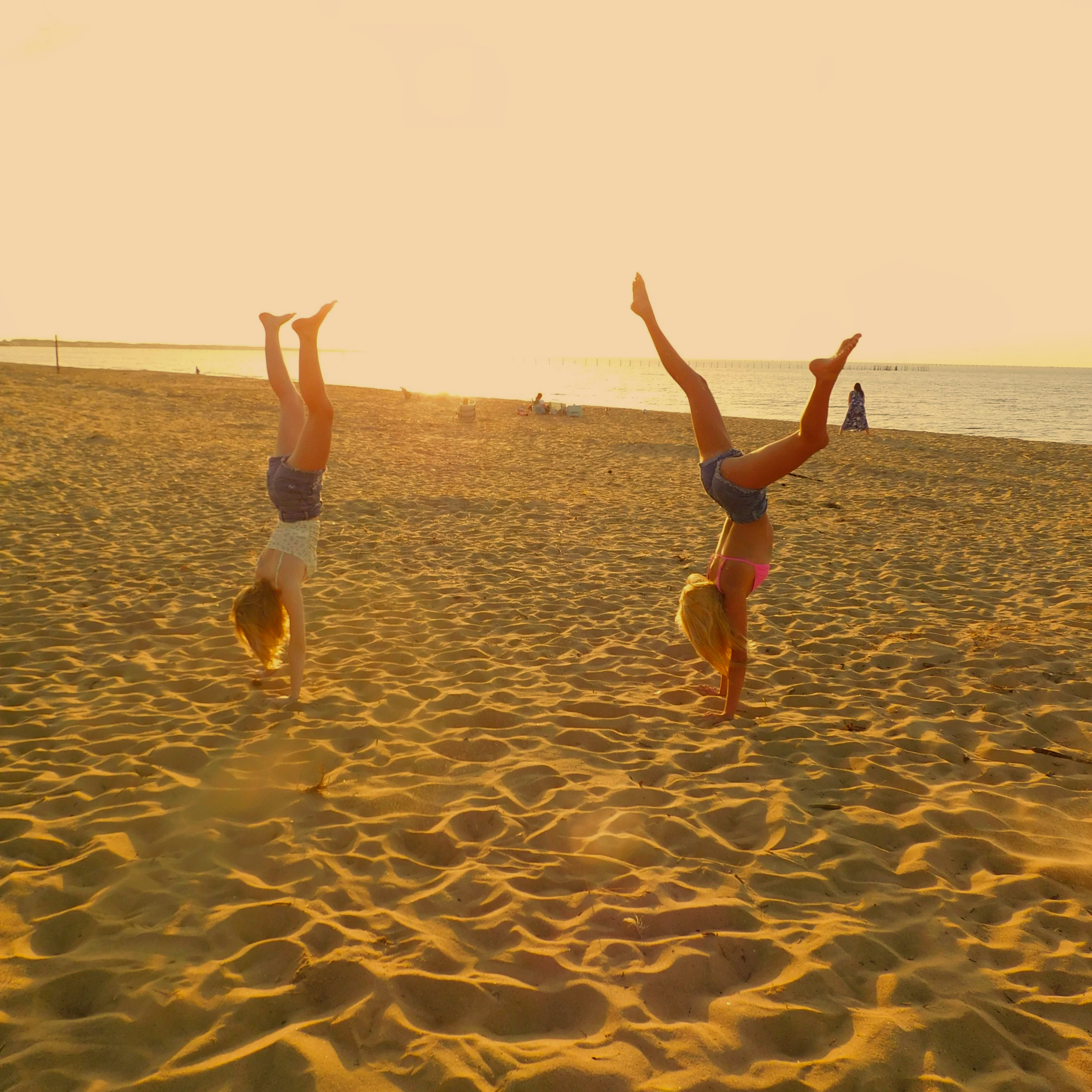 People doing handstands on the beach during sunset with their legs in the air and the sunset in the background.