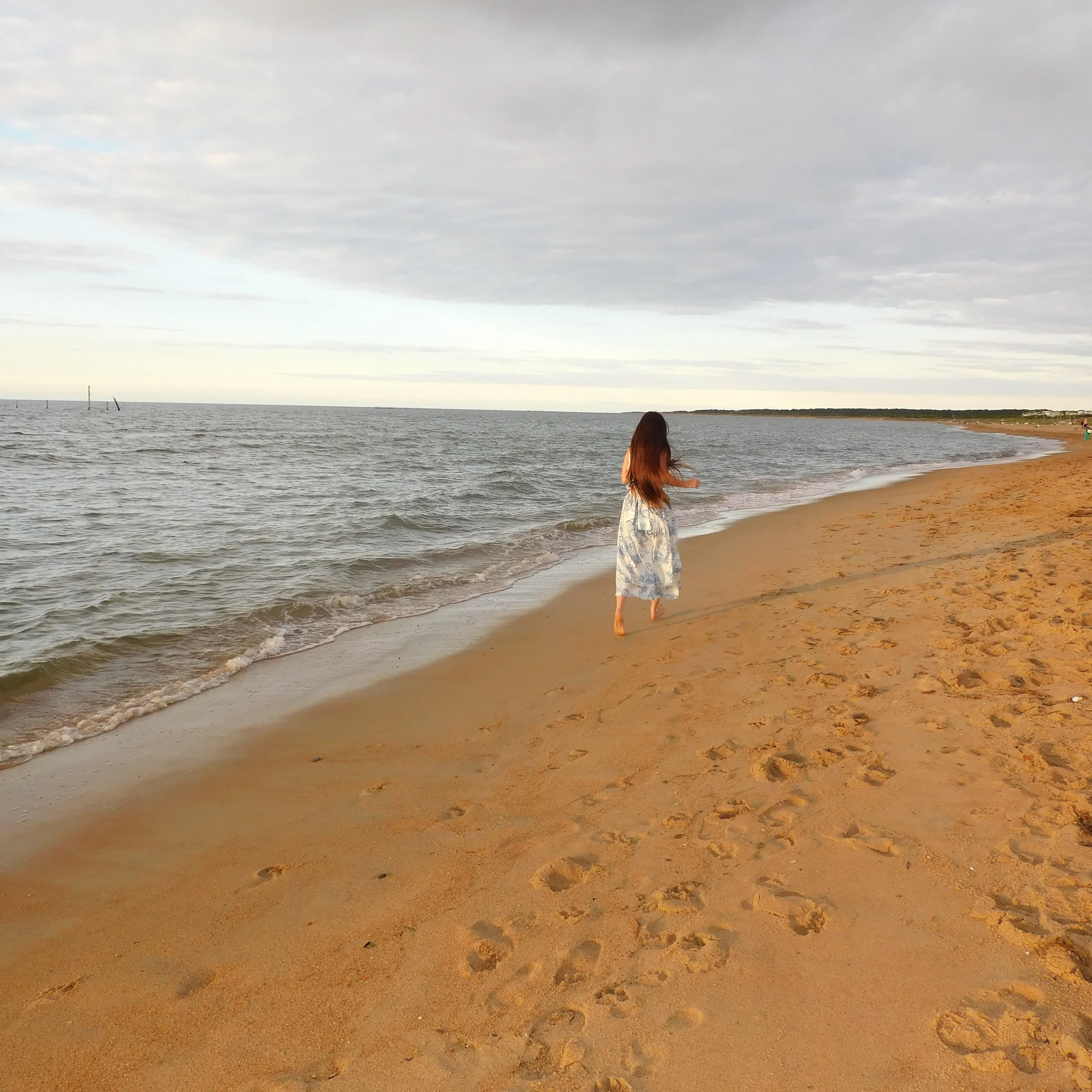 A person walking along the sandy beach near the water with a cloudy sky overhead.